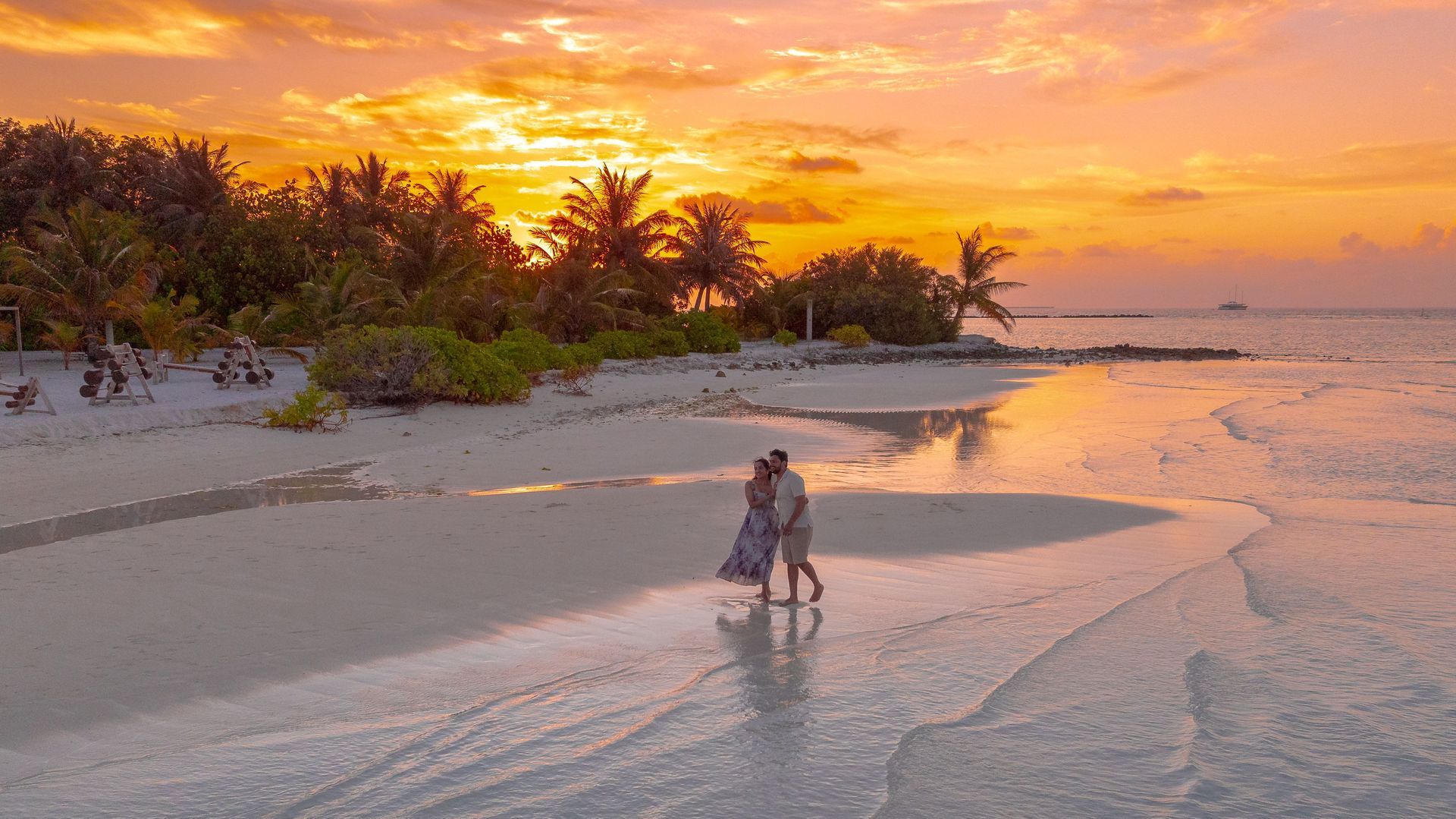 Sunset beach with palm trees and a person walking along the shoreline at low tide