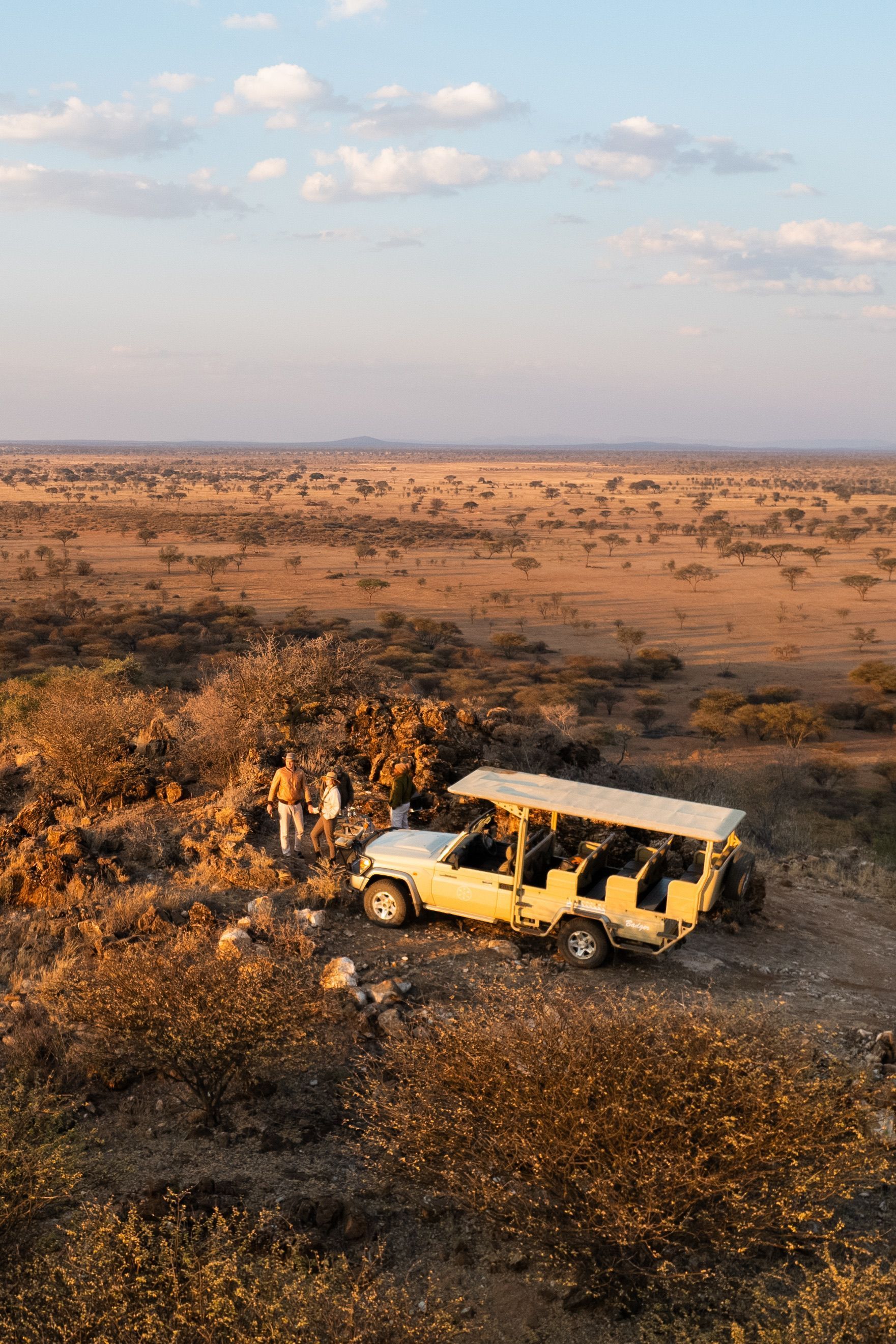 Yellow safari jeep by a tree in a dry, open savanna at sunset