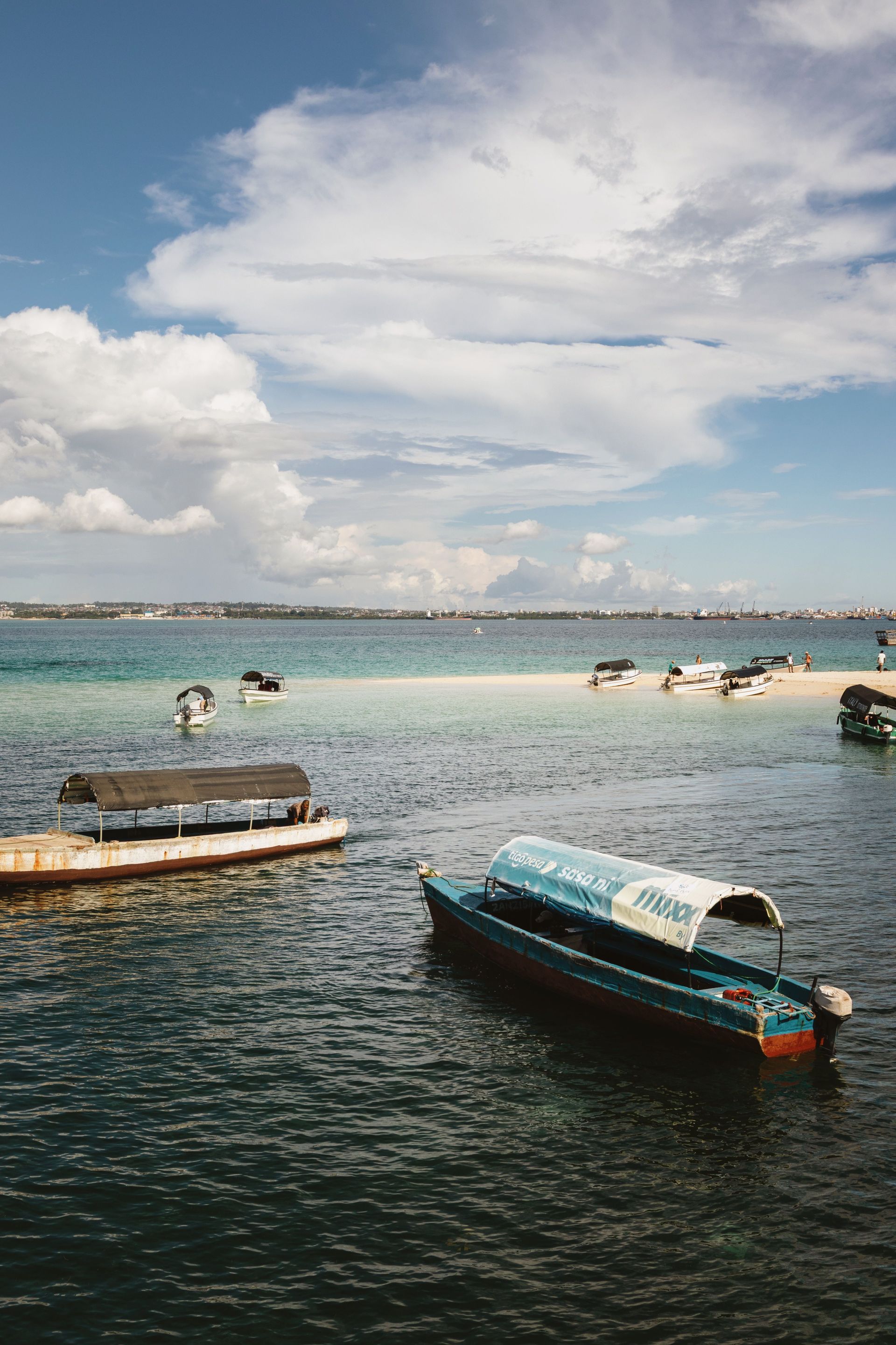 Boats floating on clear water near a shoreline under a cloudy sky