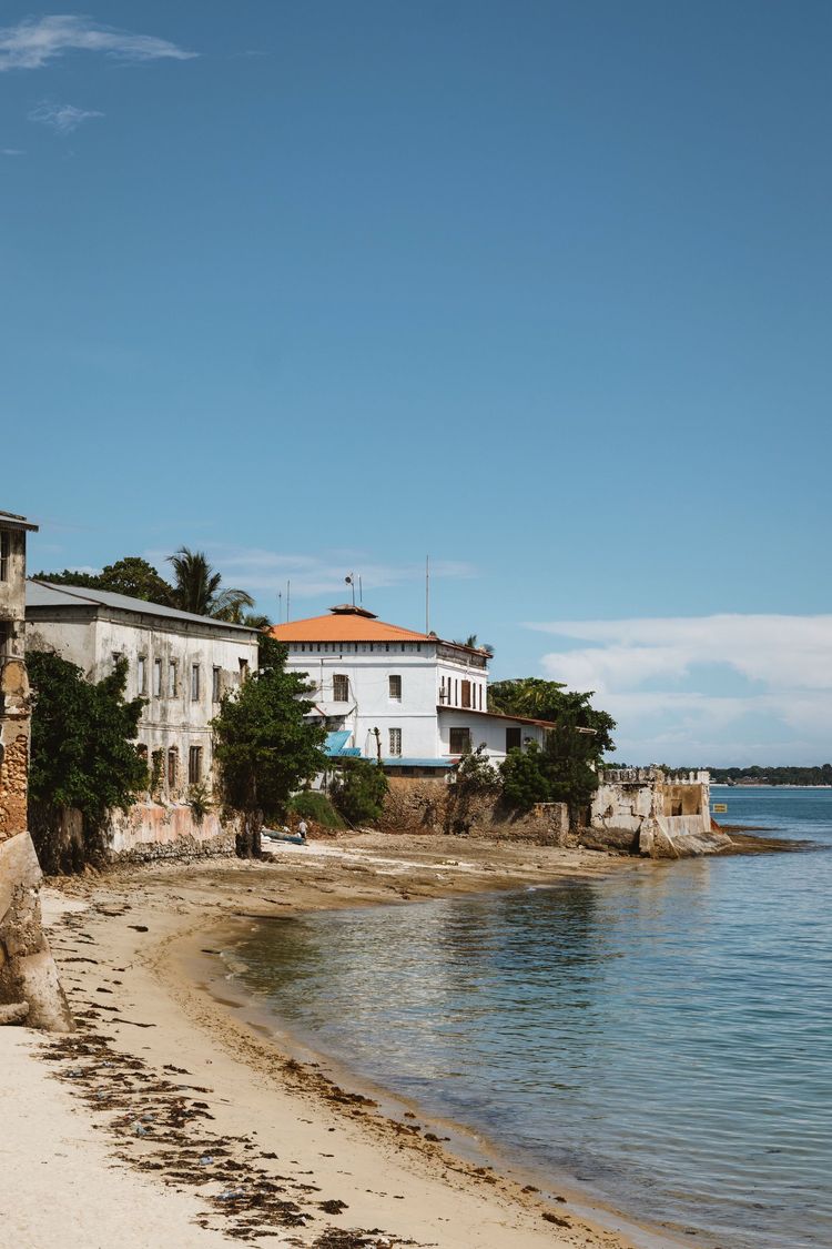 Sandy beach beside white seaside houses and calm blue water under a clear sky