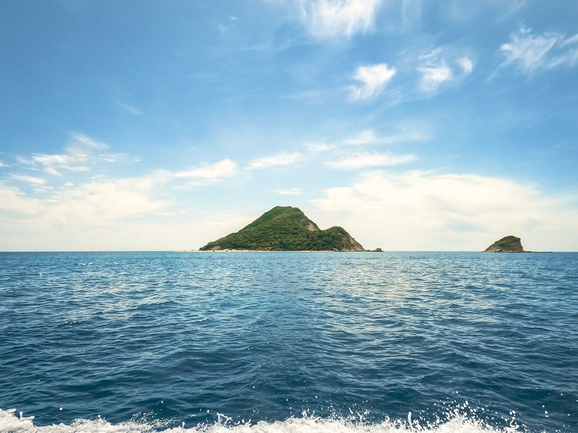 Blue ocean with two small green islands under a partly cloudy sky