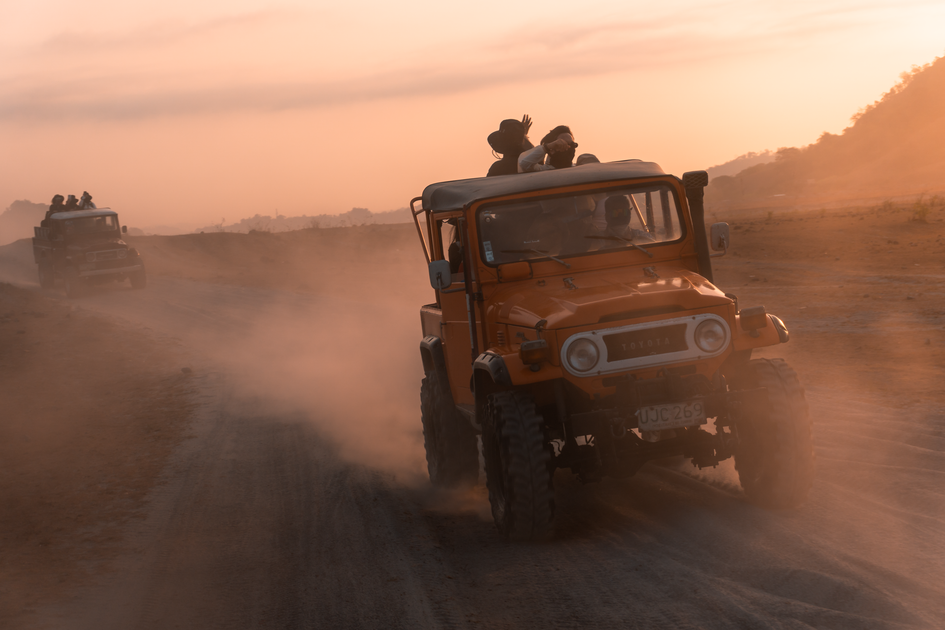 Dusty off-road vehicles racing on a dirt road at sunset
