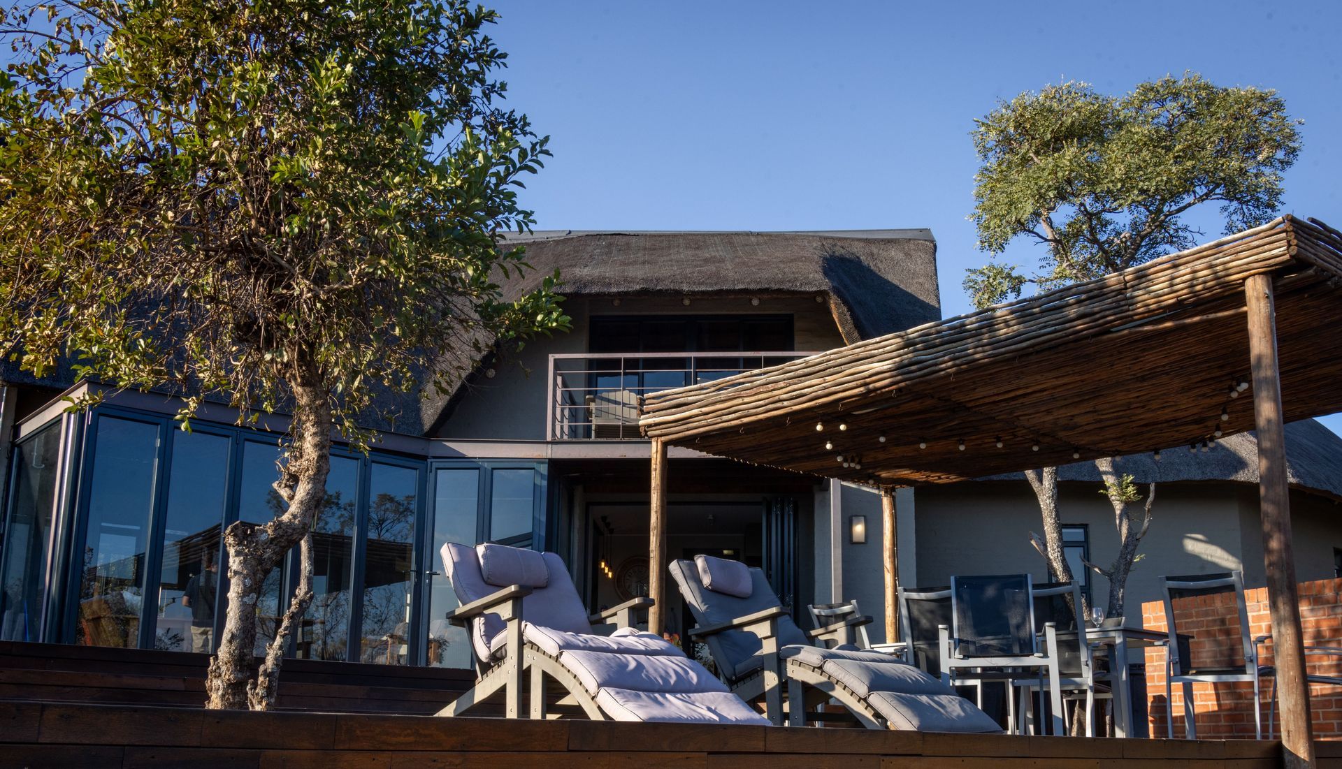 Modern house with patio seating, lounge chairs, and trees under a sunny sky