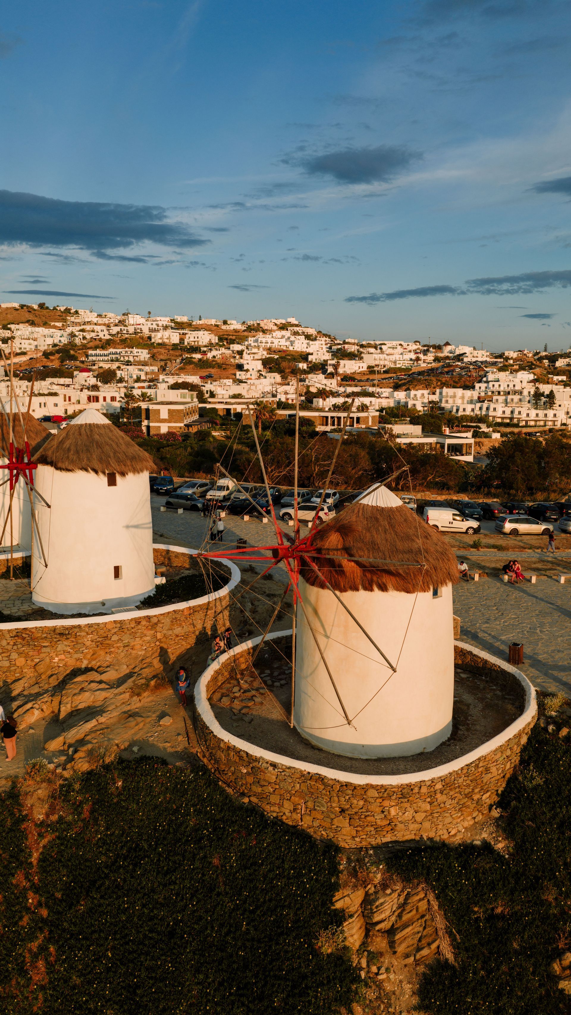 White windmills on a hillside overlooking a coastal town at sunset