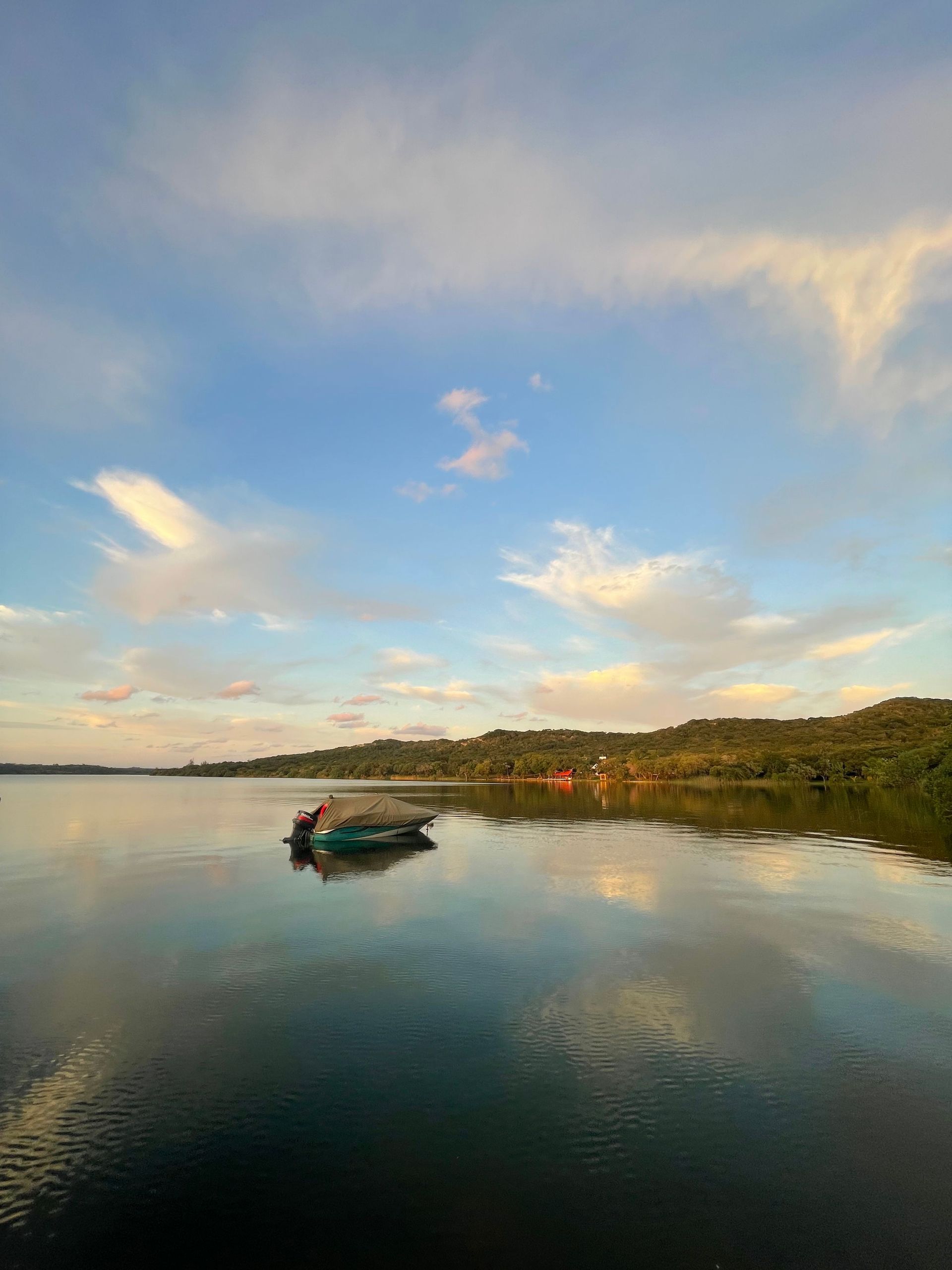 Calm lake at sunset with a small boat and a tree-lined shoreline reflected in the water