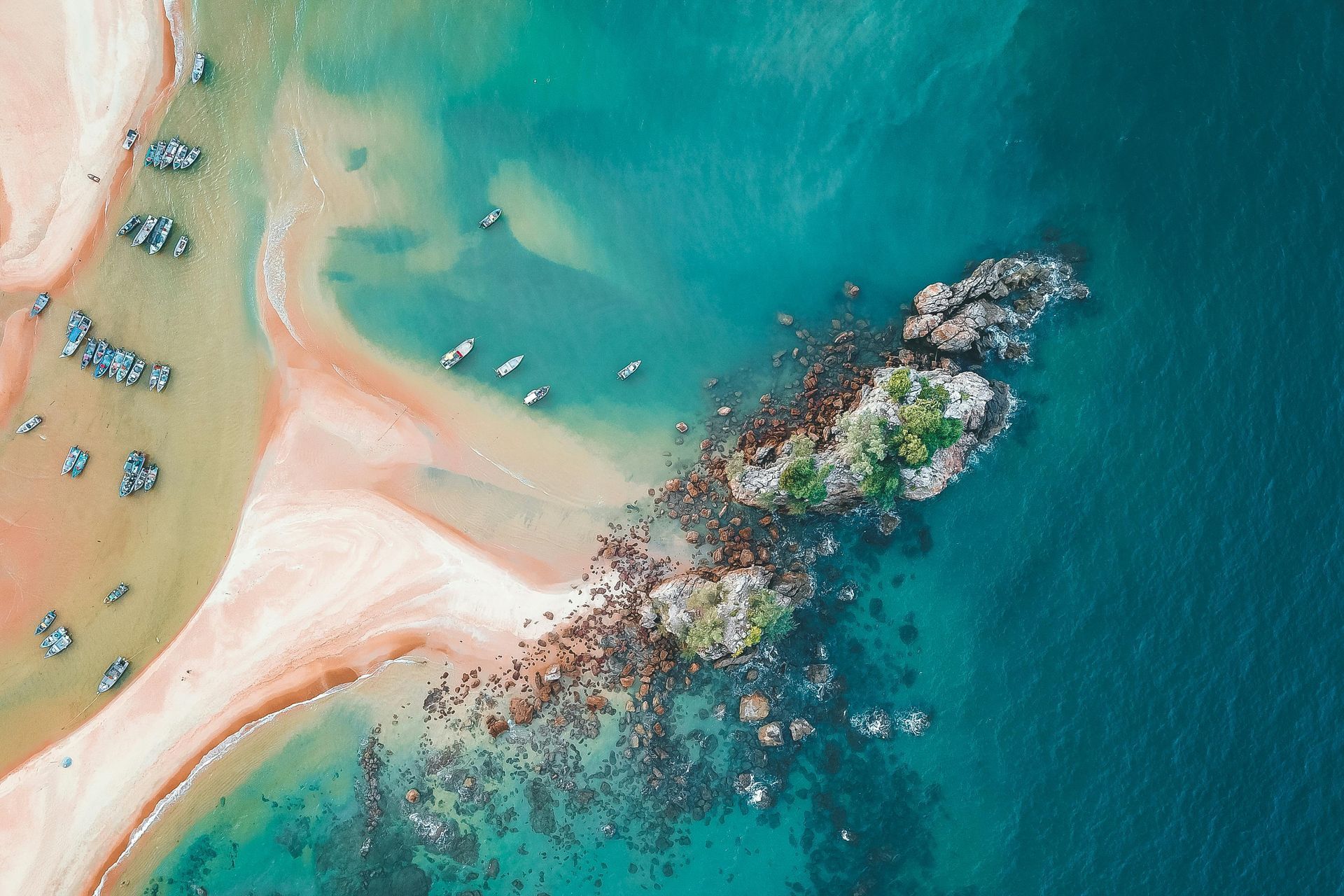 Aerial view of a turquoise beach with boats, sandy shore, and a rocky reef in clear water