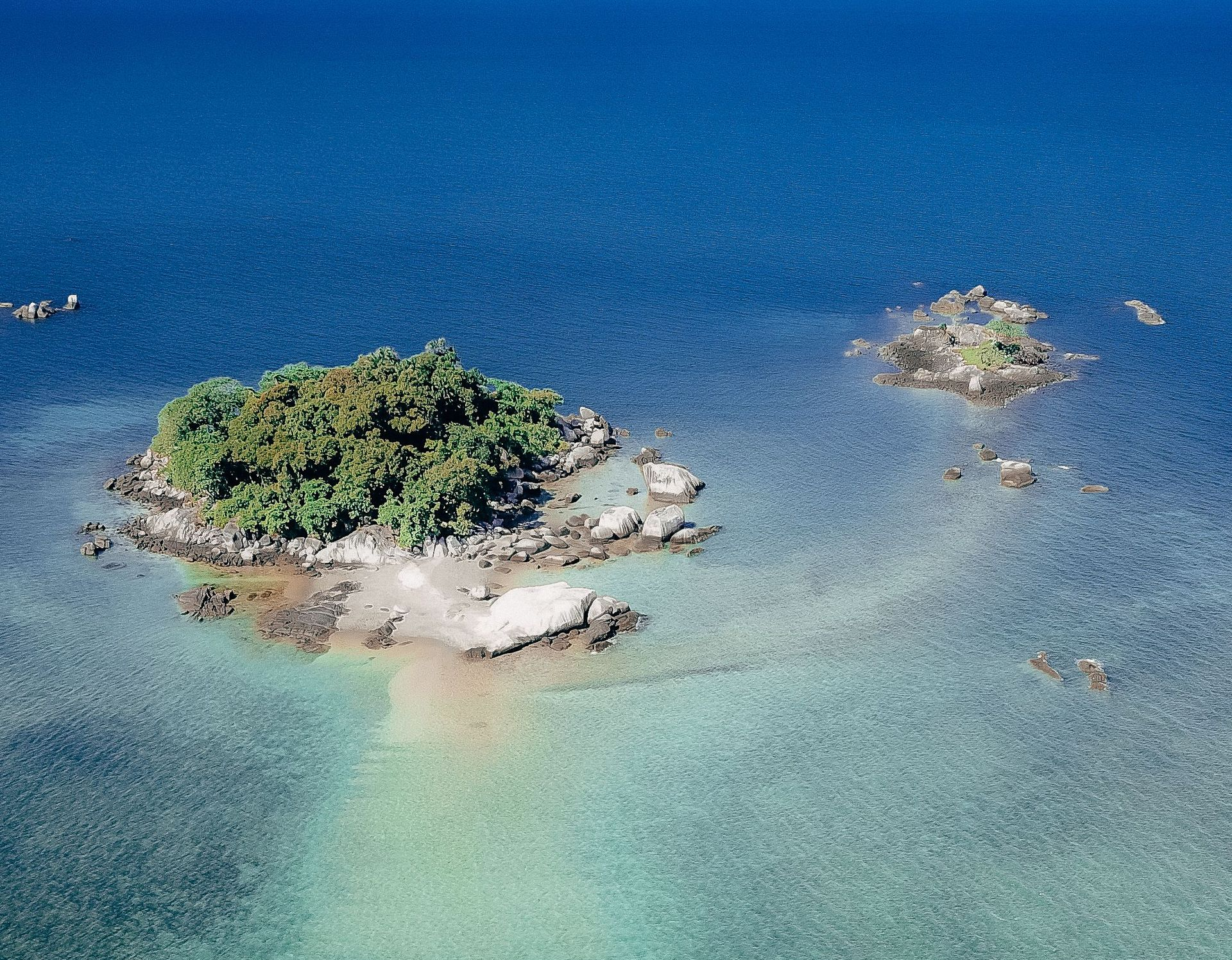 Small green island surrounded by clear turquoise water and deep blue sea.