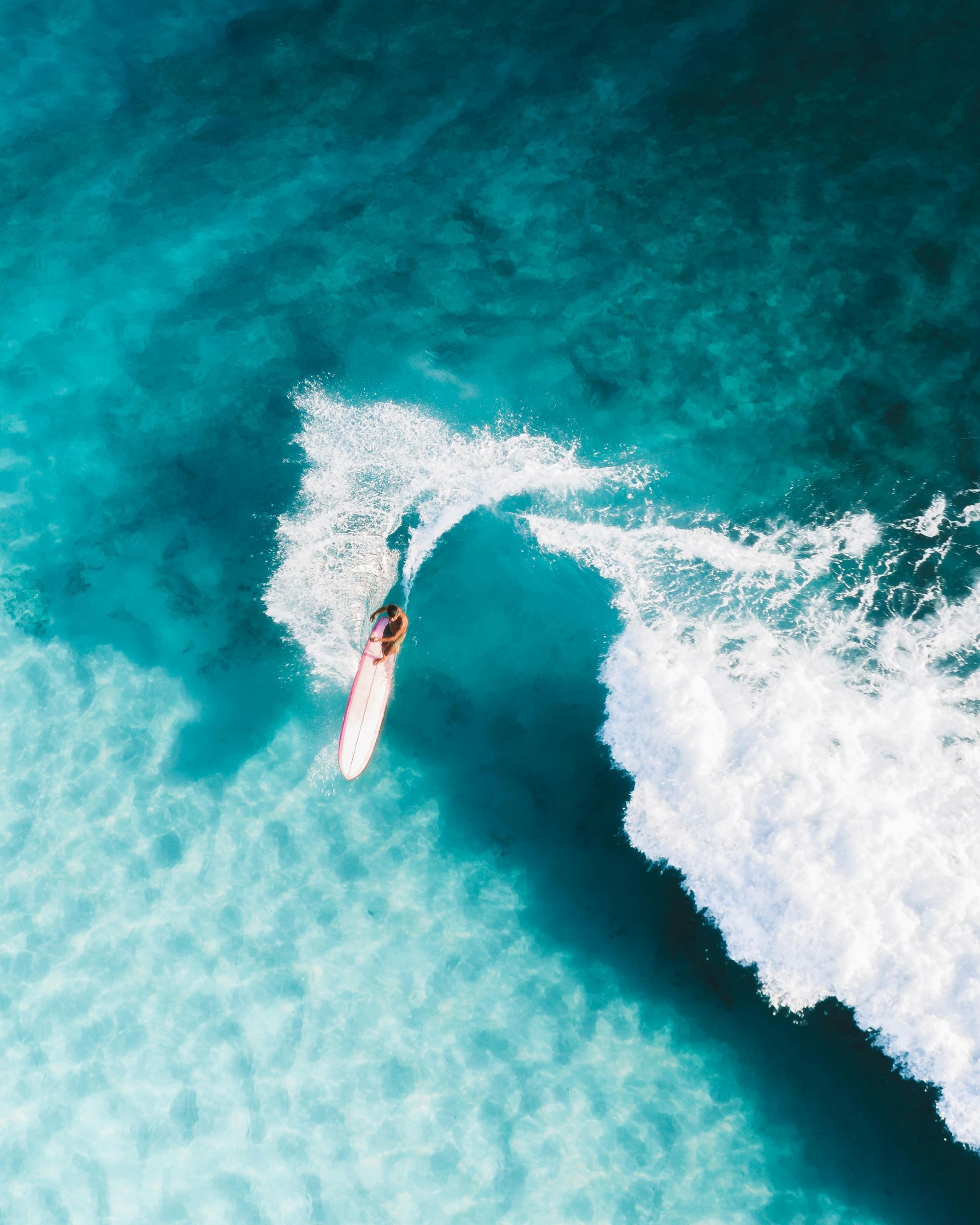 A surfer carving through turquoise waves, leaving a white spray trail.