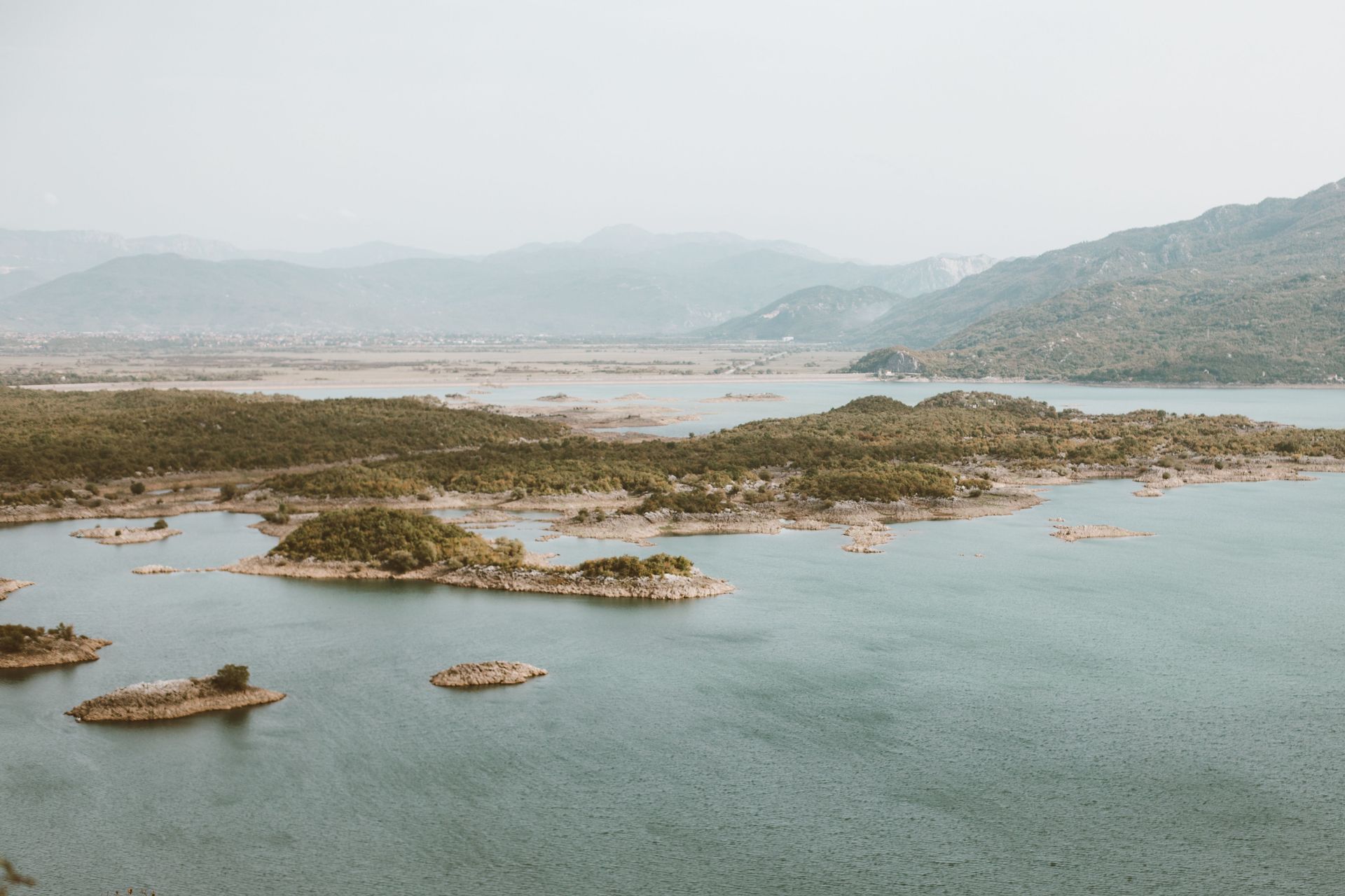 Rocky islands scattered across a calm blue lake with hazy mountains in the distance