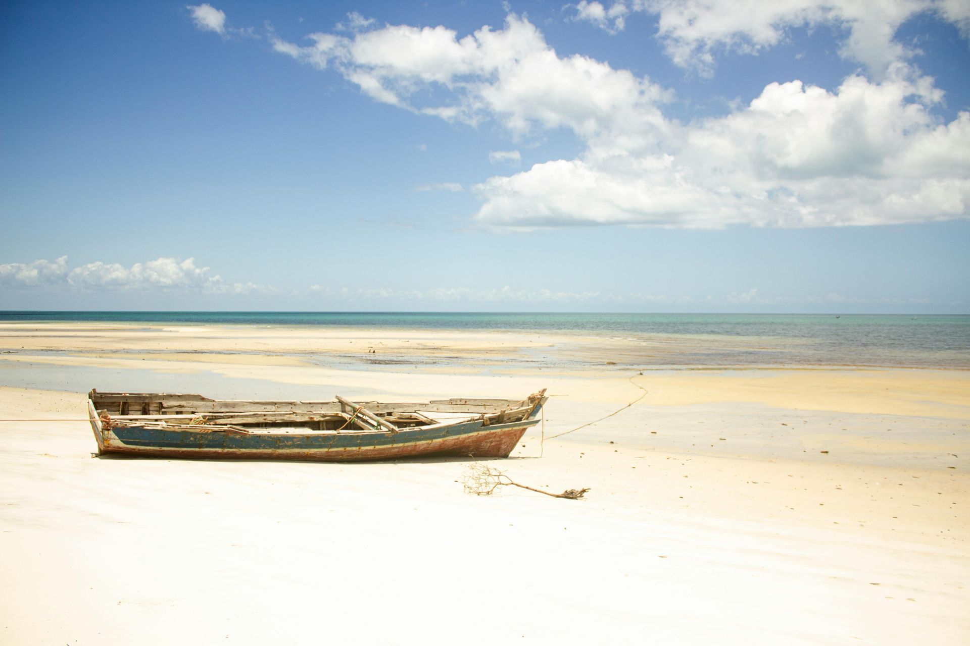 A small wooden boat resting on a bright sandy beach under a blue sky and calm sea