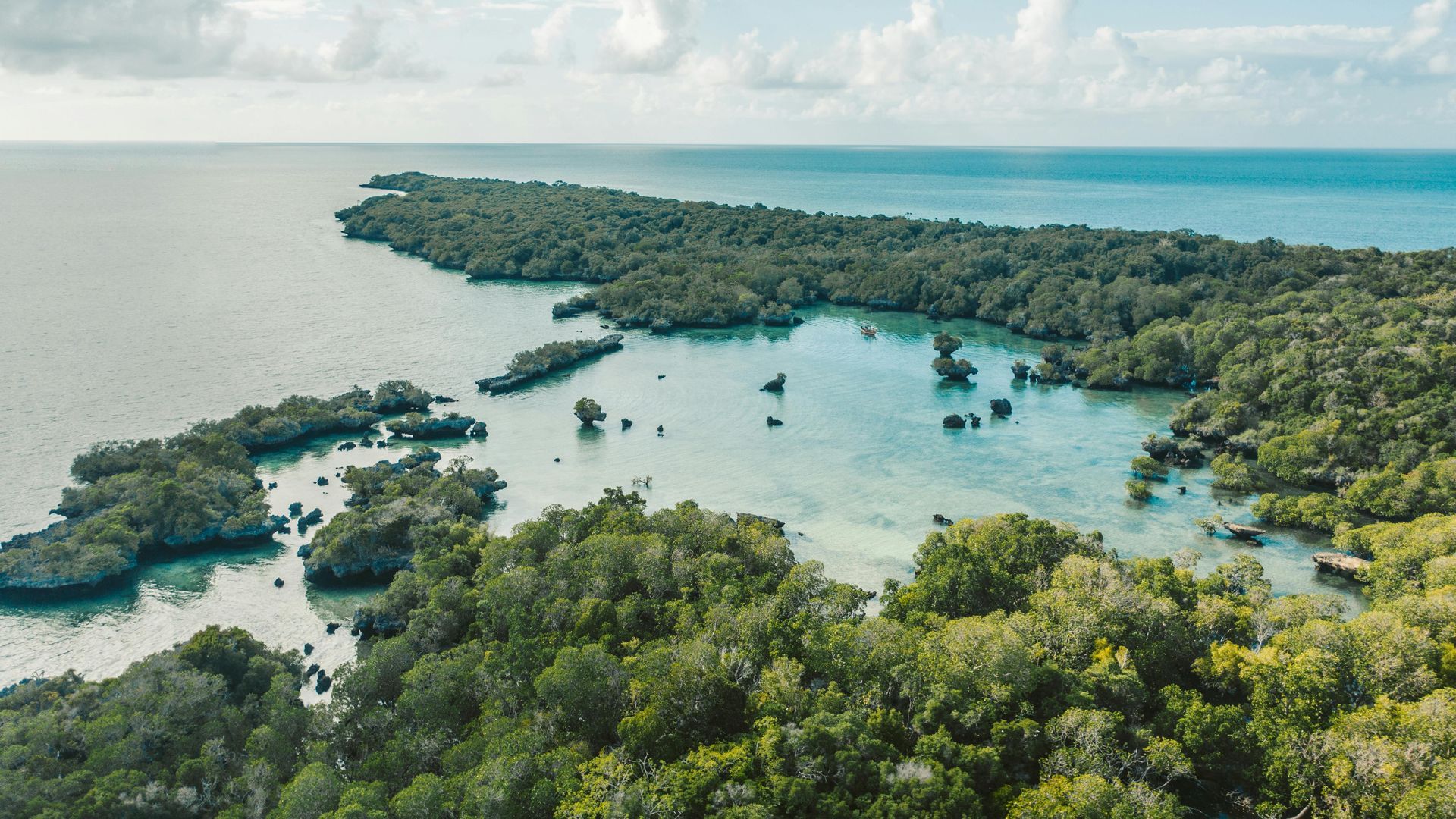Aerial view of a lush tropical island lagoon with turquoise water and scattered mangroves beneath a cloudy sky