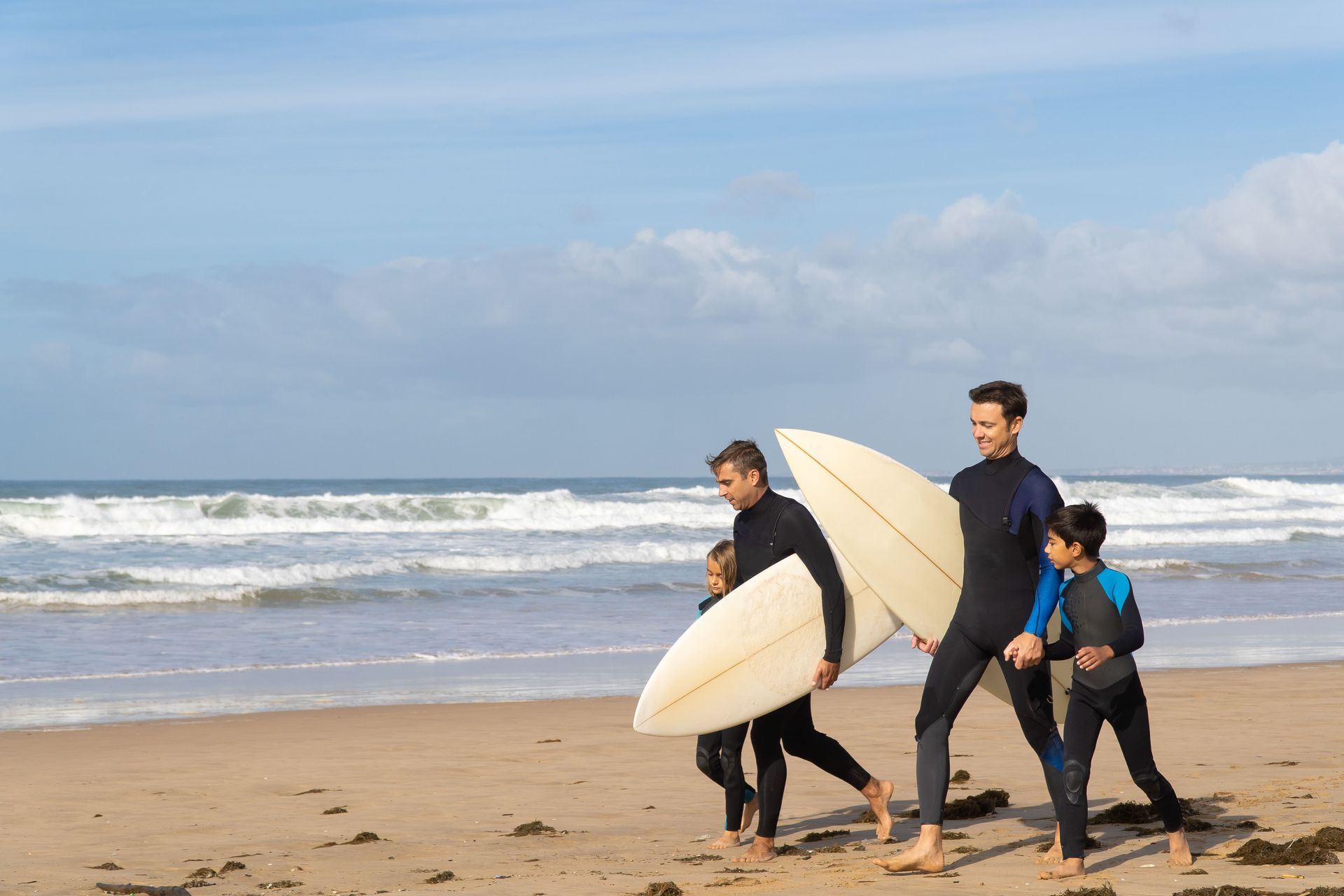 People carrying surfboards along a sandy beach with waves in the background