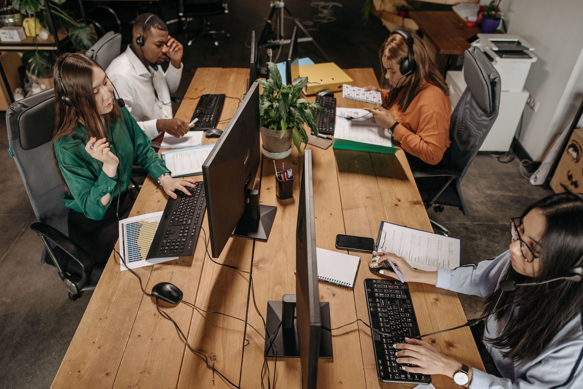 Four people working at laptops in a shared office around a long wooden table