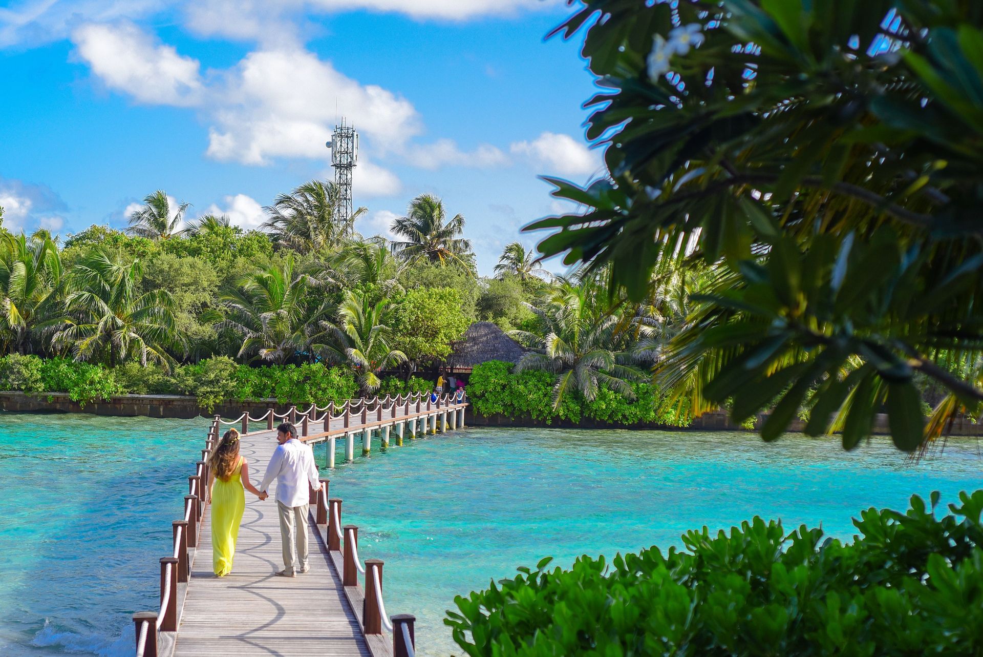 People walking on a wooden bridge over bright turquoise water toward a lush tropical island