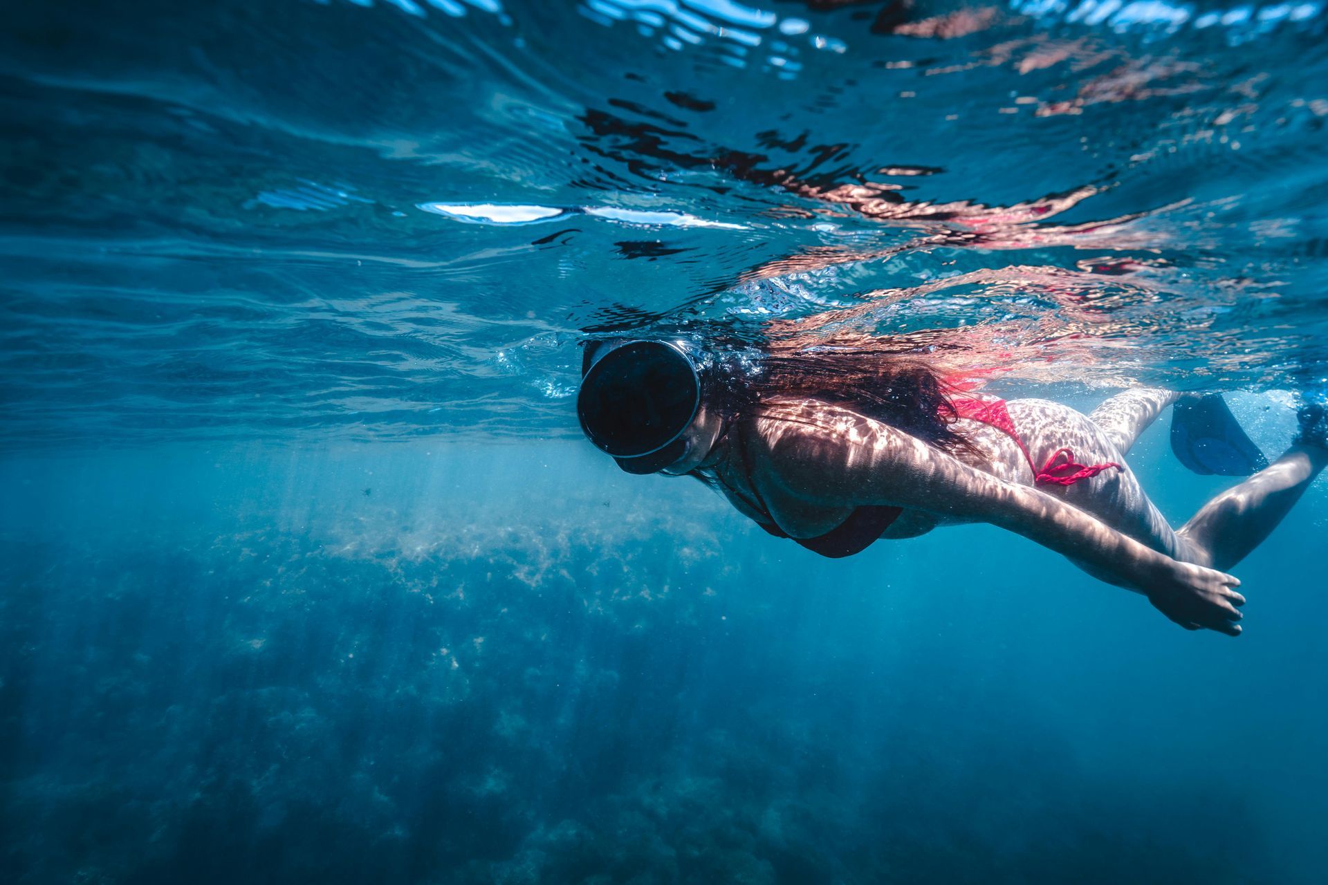 Person swimming underwater in a blue ocean, wearing a pink top and black shorts