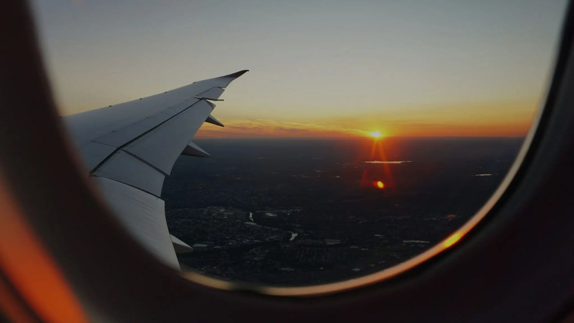 View from airplane window of wing over sunset sky and distant horizon