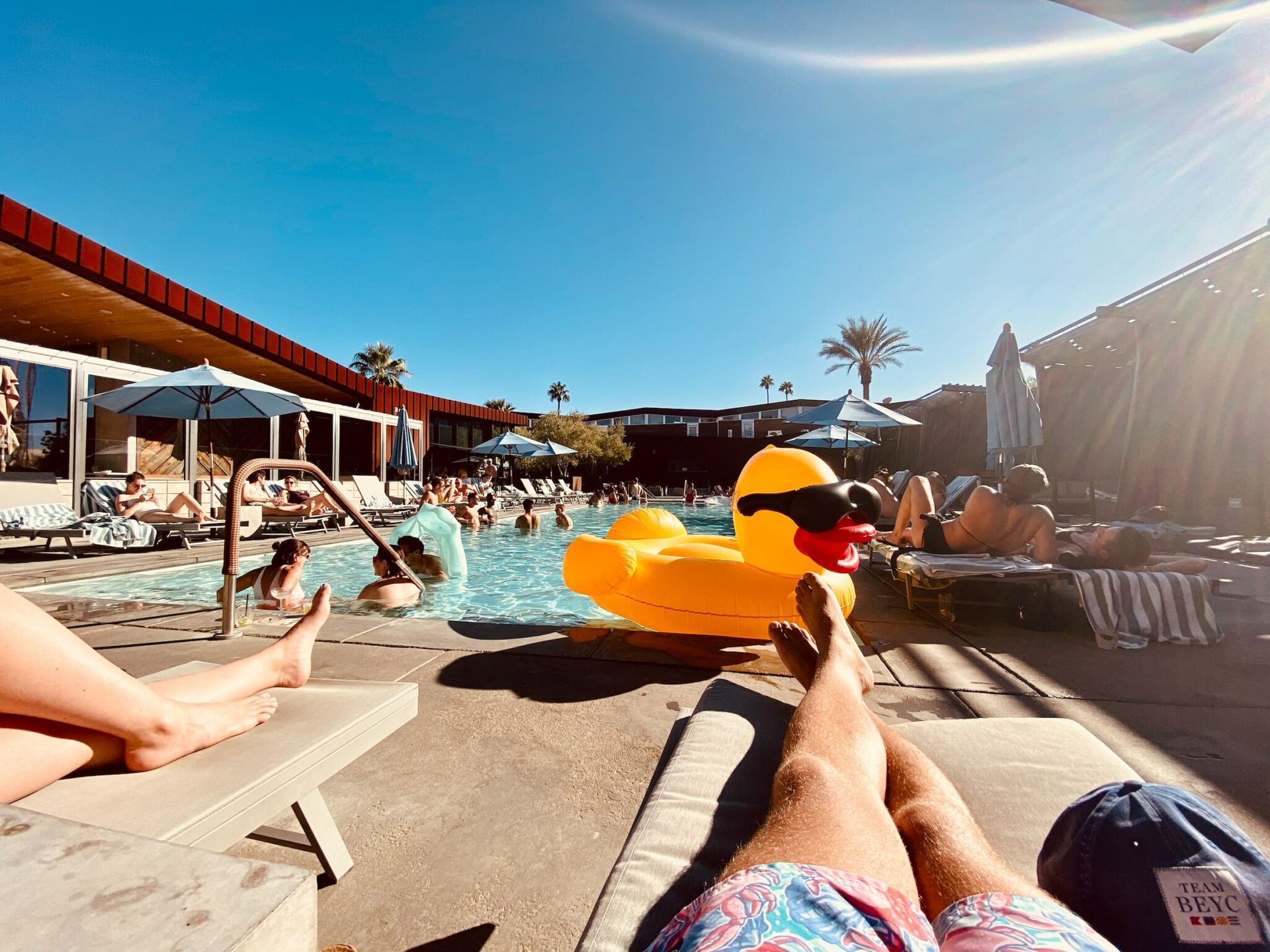People lounging by a pool with a bright yellow float in a sunny resort area