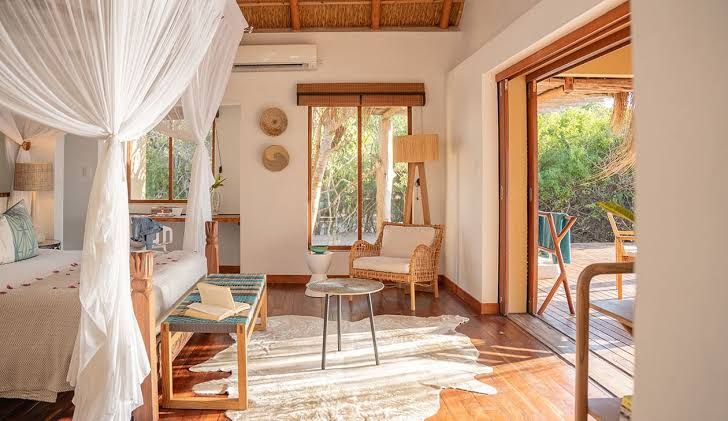 Bright, airy living room with white curtains, wooden furniture, and an open doorway to a sunny patio