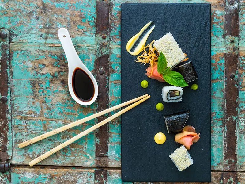 Sushi platter with chopsticks and soy sauce on a dark slate board over a rustic turquoise table