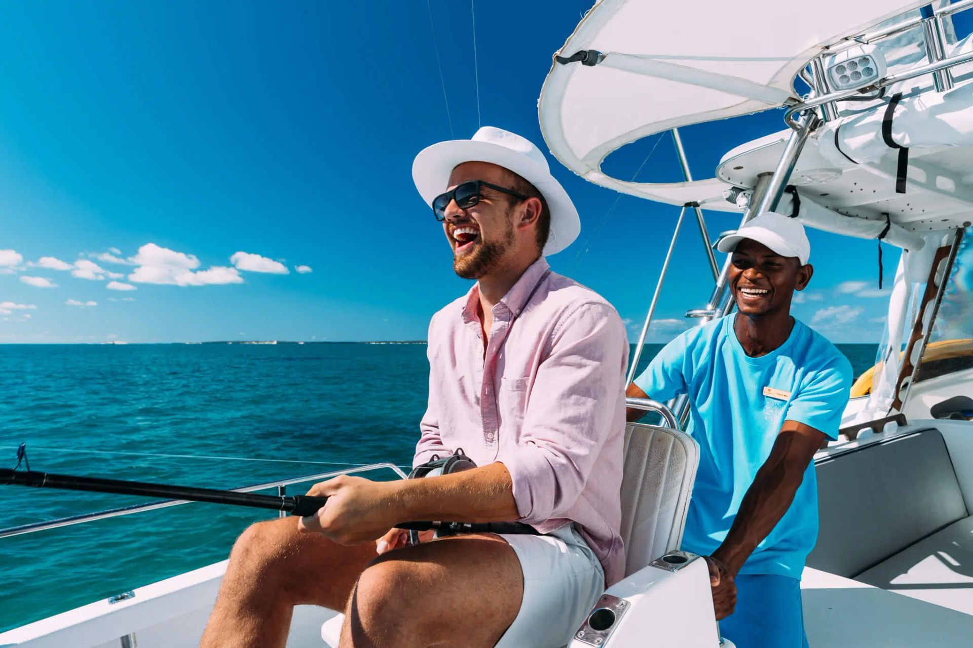 Two men sailing on a boat, smiling under a white canopy on a bright blue ocean