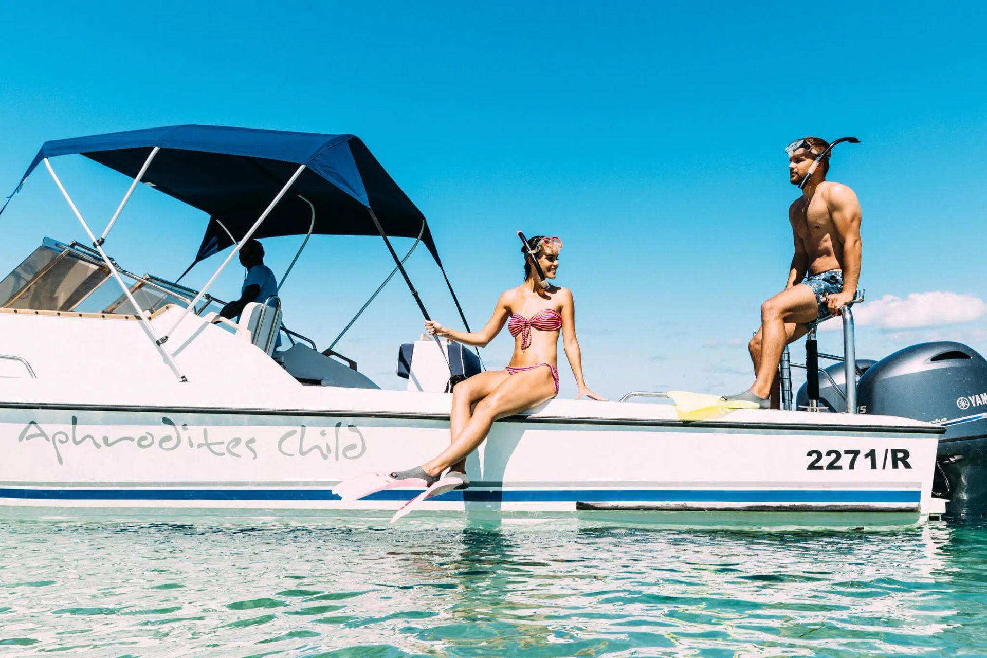 Two people relaxing on a white boat in clear turquoise water under a blue sky.