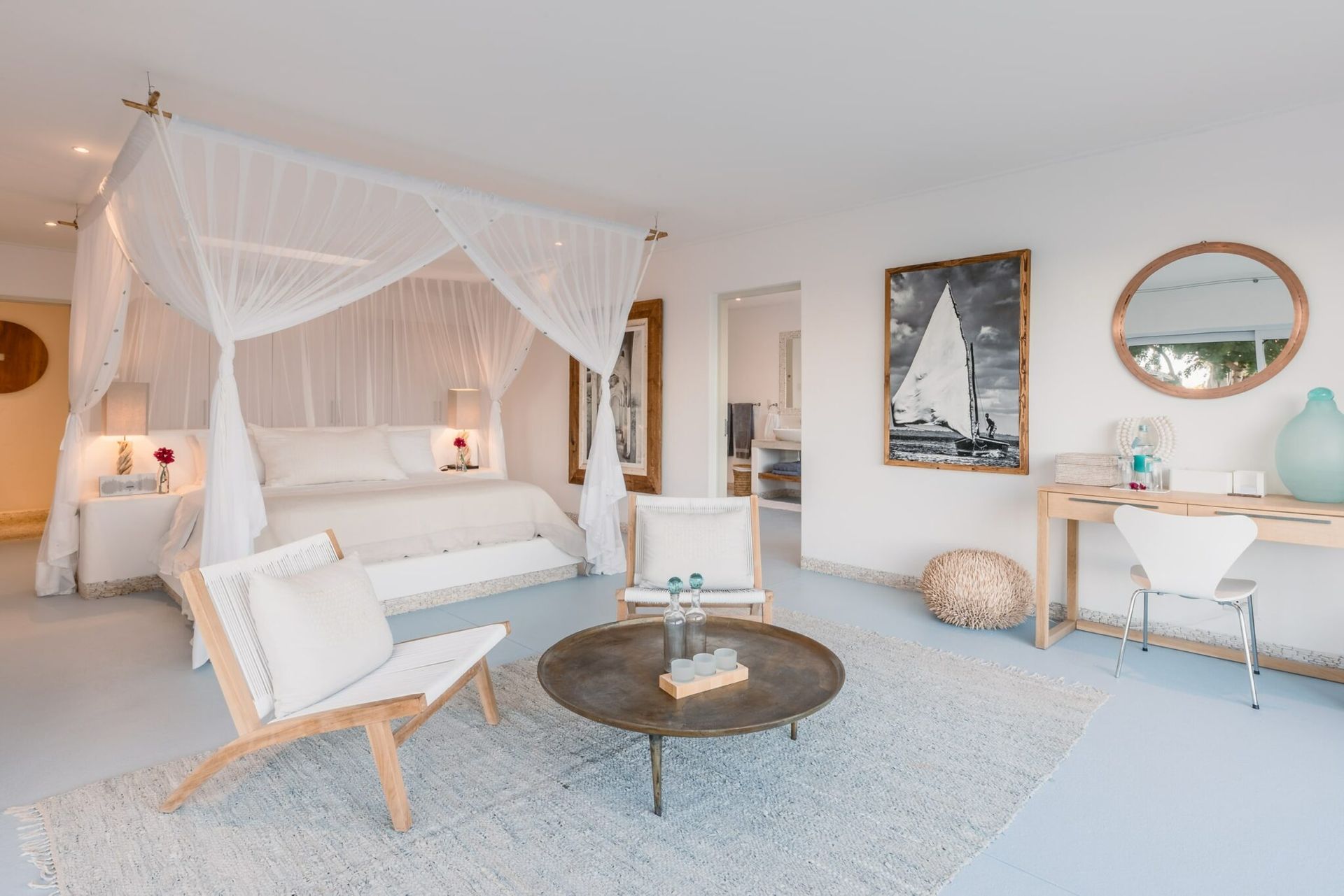 Bright airy bedroom with canopy bed, white decor, lounge chair, and vanity