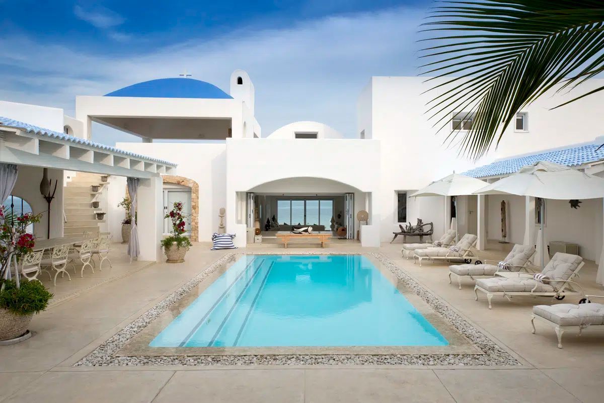 White villa courtyard with turquoise pool, lounge chairs, and blue-domed roof under a bright sky