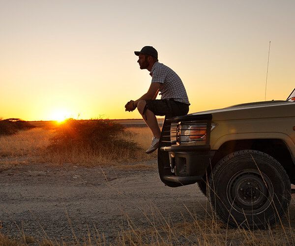 Silhouette of a person sitting on a pickup truck bumper at sunset in a rural field