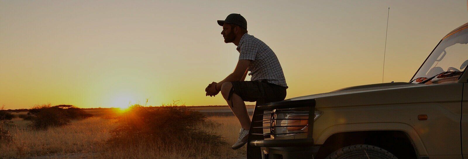 Silhouetted person sitting on a pickup truck at sunset in a dusty desert landscape