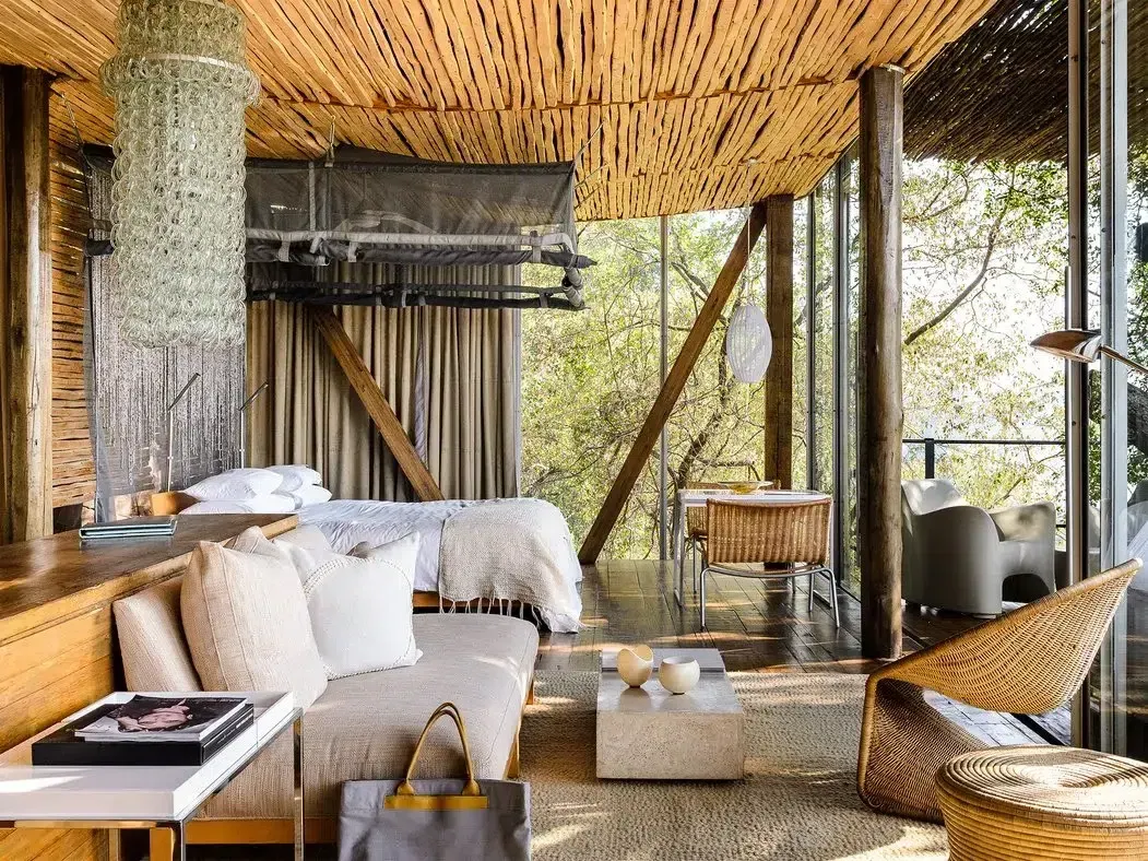 Rustic open-air lounge with wicker furniture, white cushions, and woven ceiling overlooking greenery