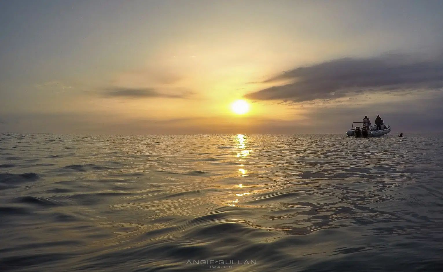 Sunset over calm ocean with a small boat silhouetted on the horizon