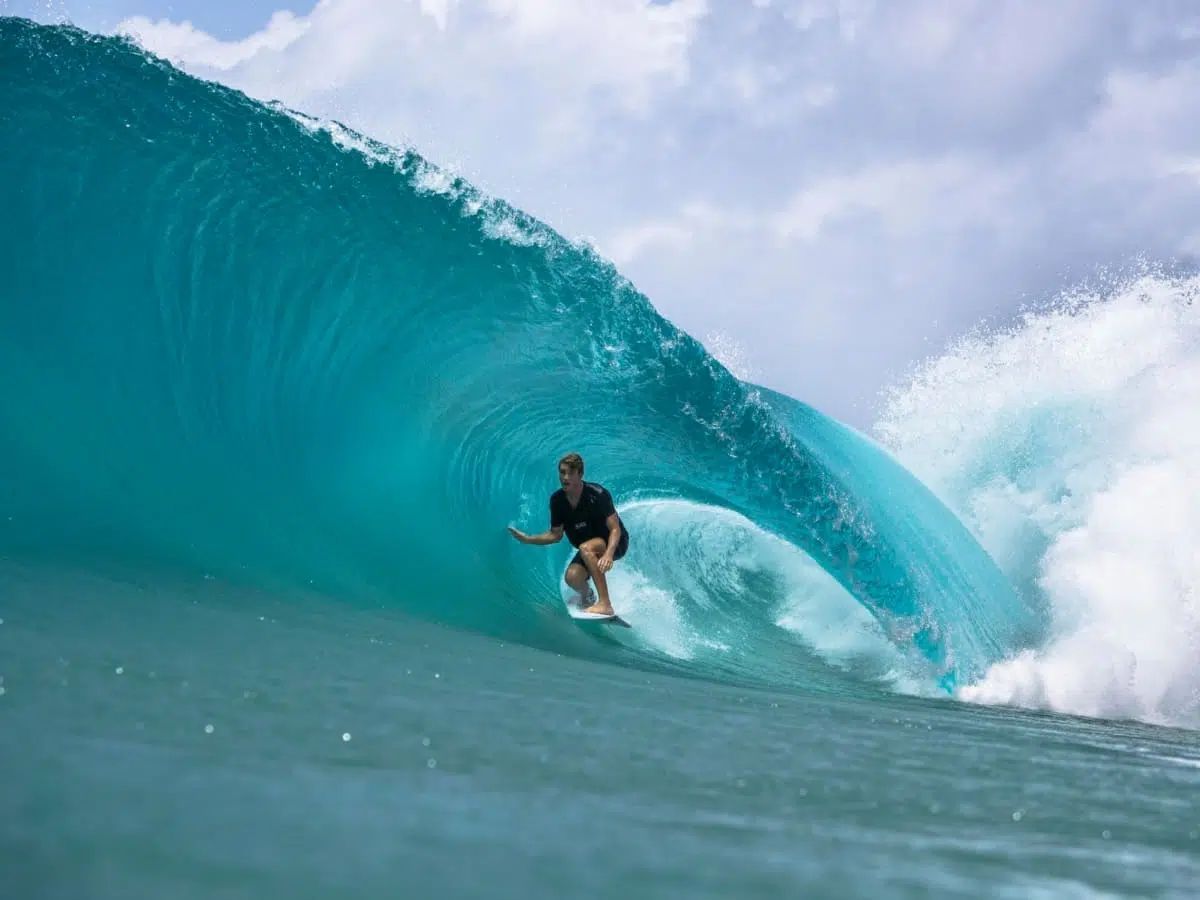 Surfer riding inside a turquoise wave with spray curling overhead