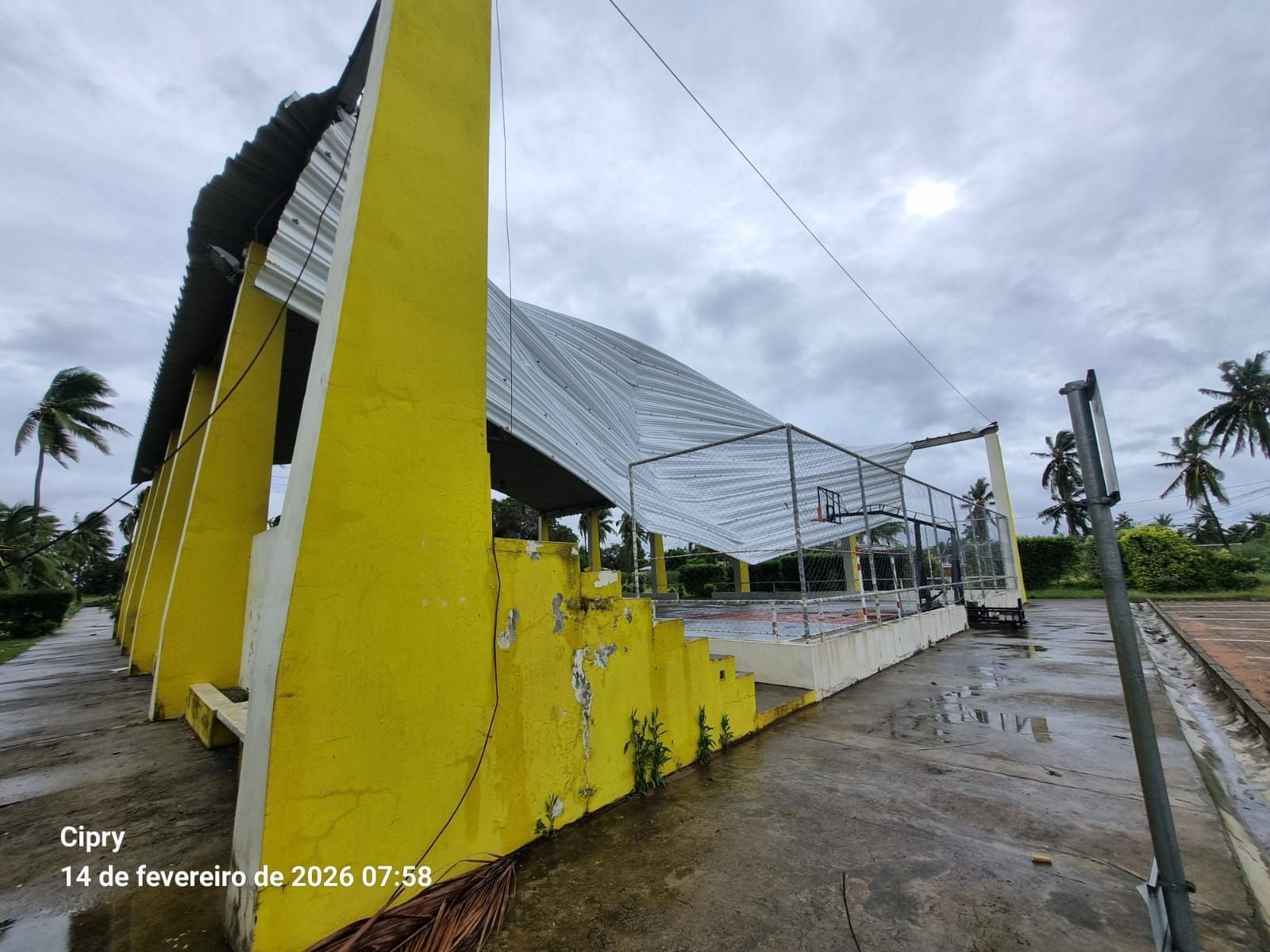 Yellow building with a metal roof beside a wet road under a cloudy sky