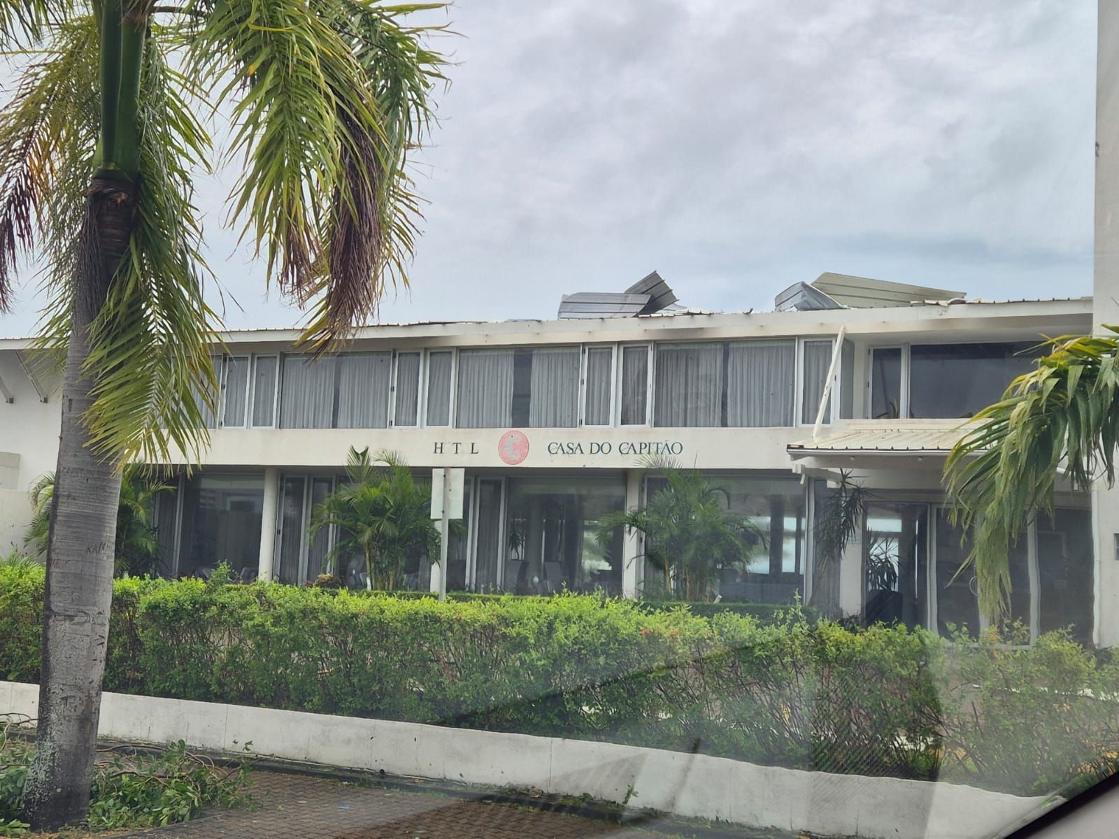 Low white building with palm trees and trimmed hedges under a cloudy sky