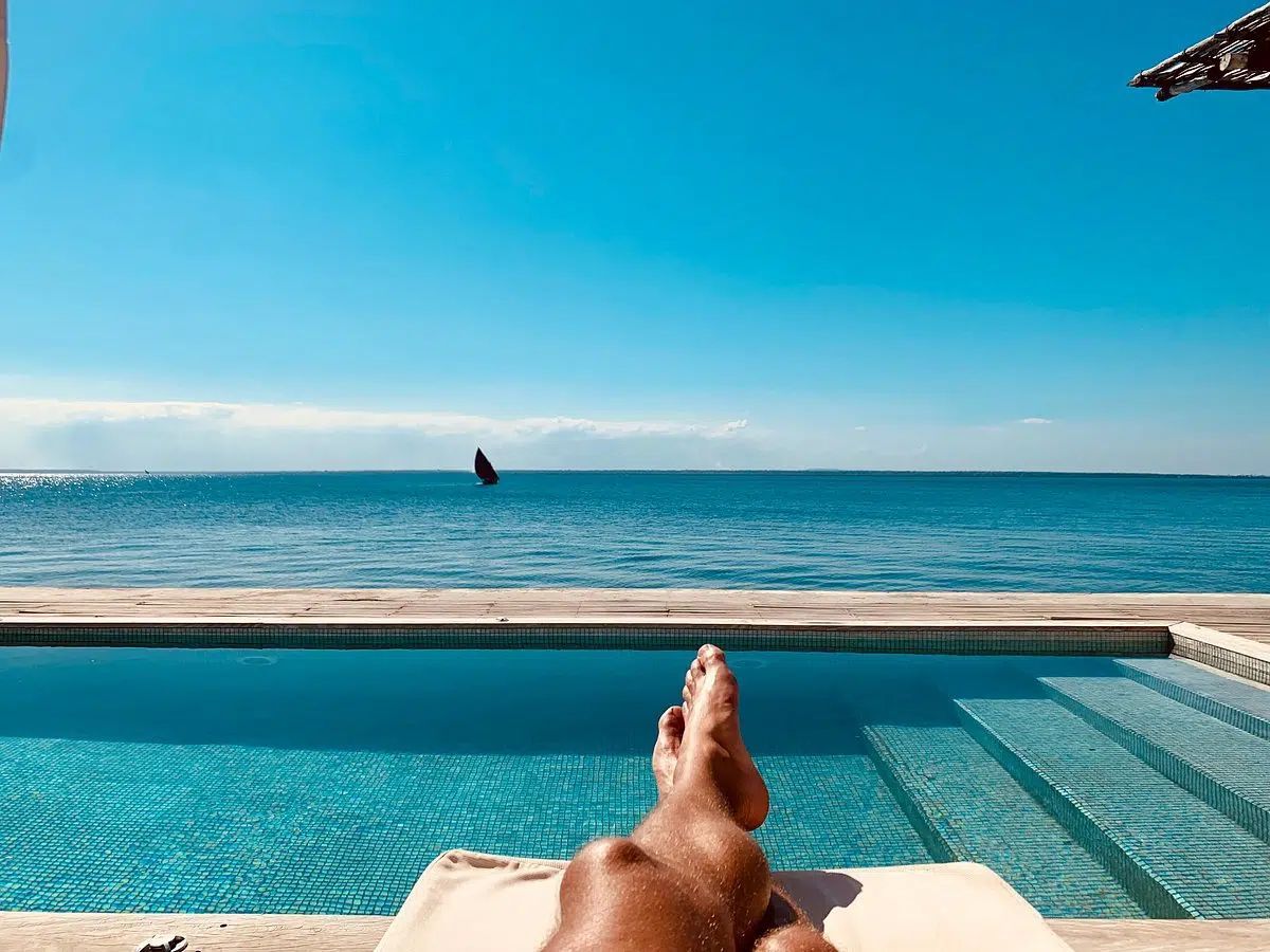 Poolside lounge chair facing a turquoise infinity pool and calm ocean under a clear blue sky.