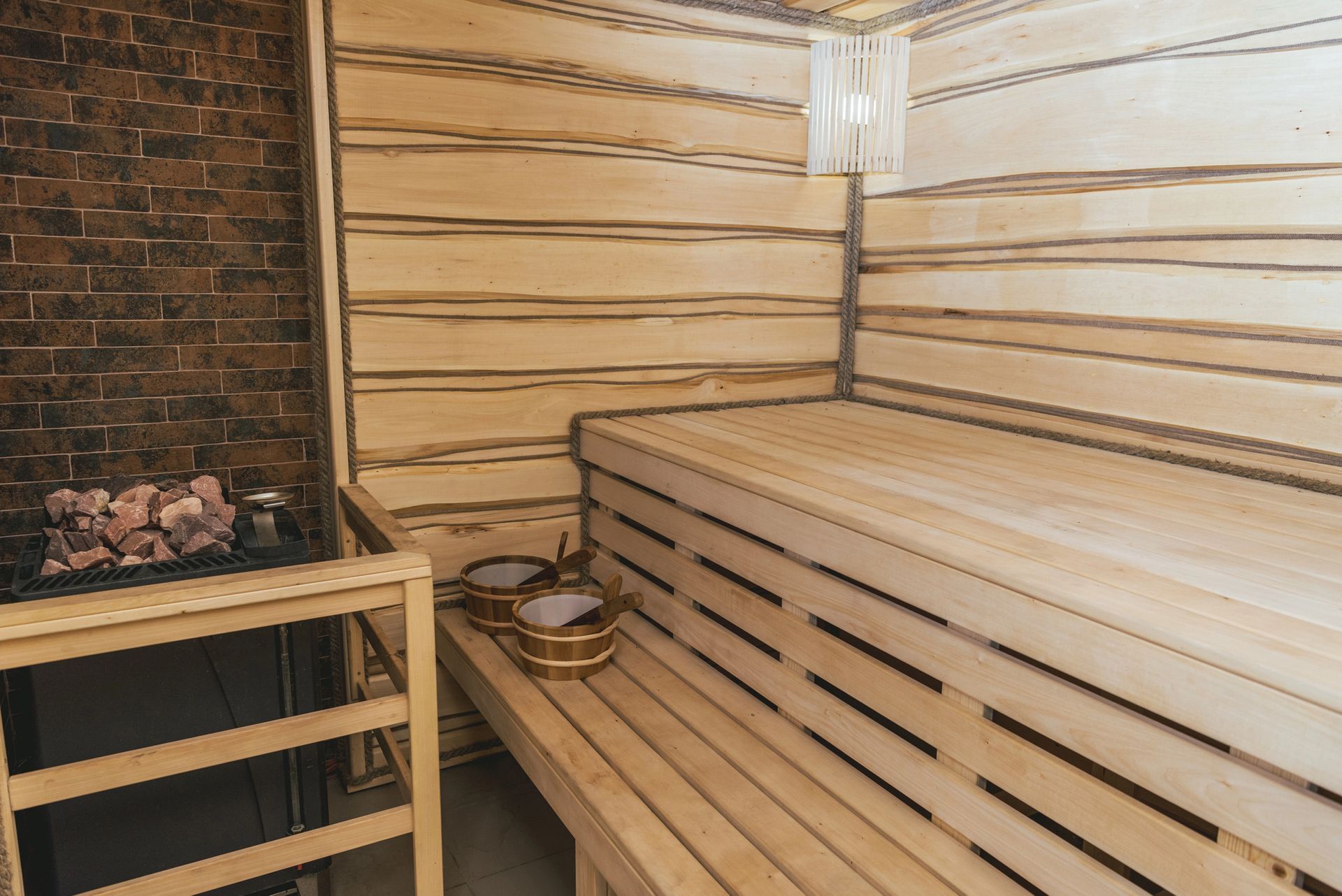 Sauna revestida de madera con bancos de madera, estufa de ladrillo e iluminación interior cálida.