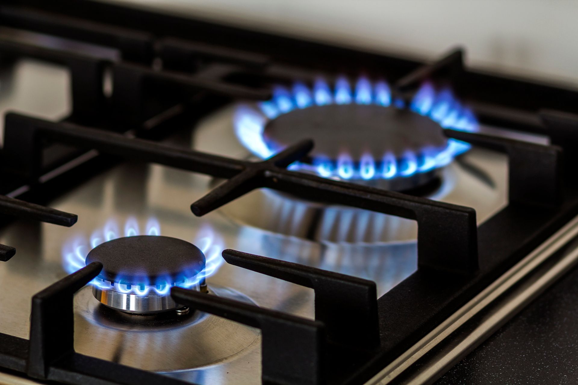 Dos quemadores de gas encendidos con llamas azules sobre una placa de cocción de acero inoxidable.