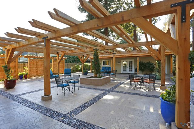 A wooden pergola with tables and chairs underneath it