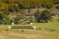 A rectangular plot of land highlighted by map markers on a grassy meadow, with trees and hills in the background.