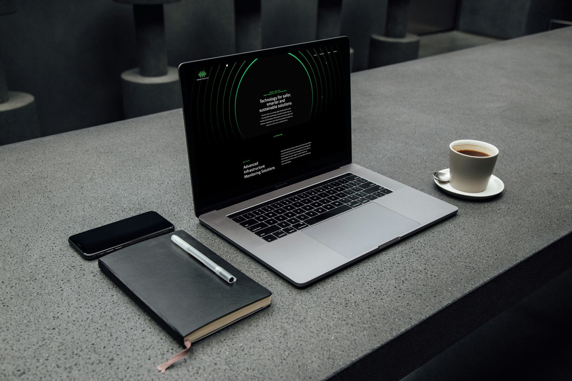 Laptop, notatbok og kaffe på et mørkegrått steinbord.