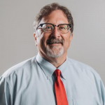 A man wearing glasses and a red tie is smiling for the camera.