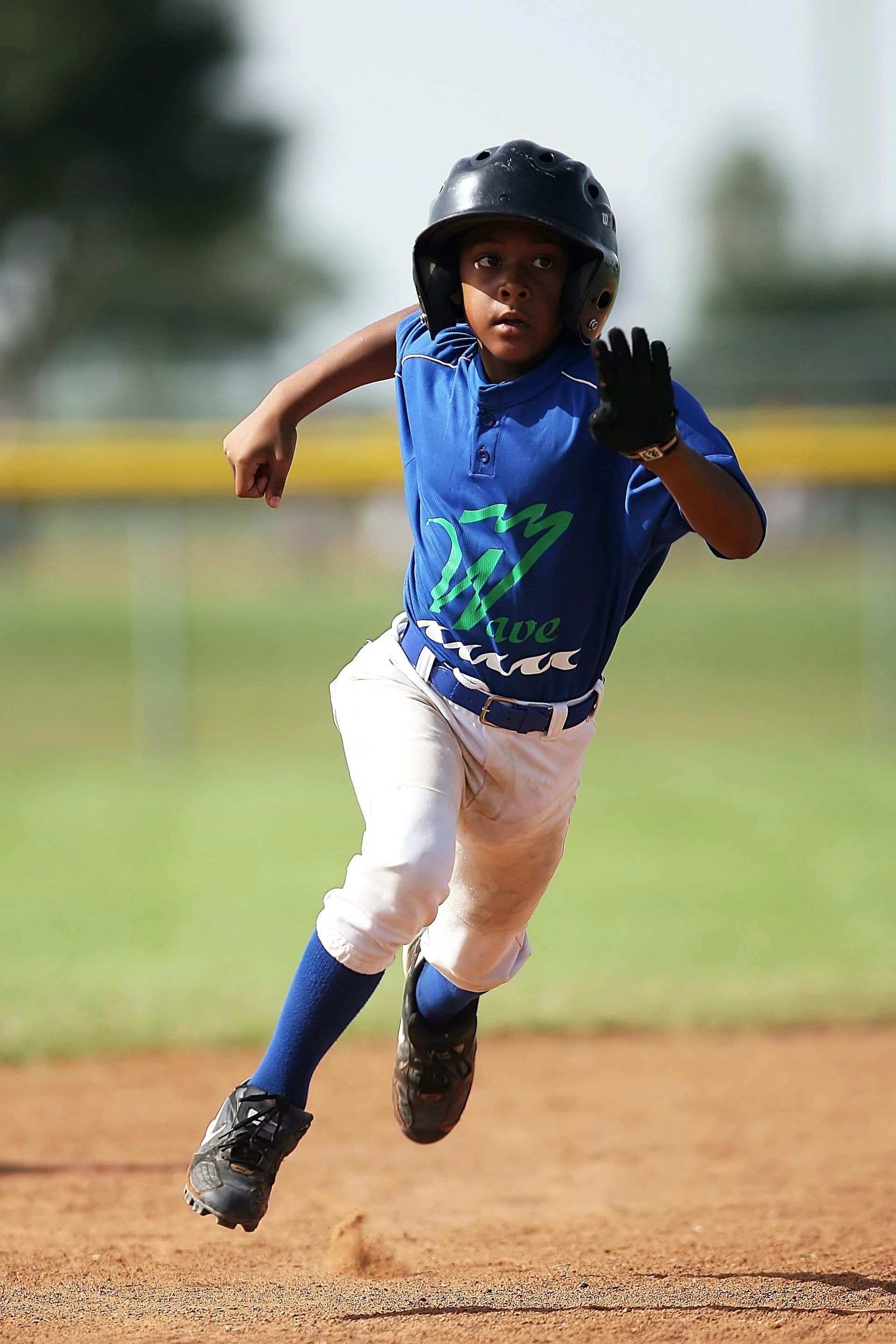 A young boy in a blue shirt and white pants is running on a baseball field.