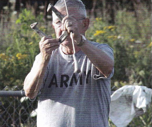A man in an army shirt is holding a hammer and a wrench.