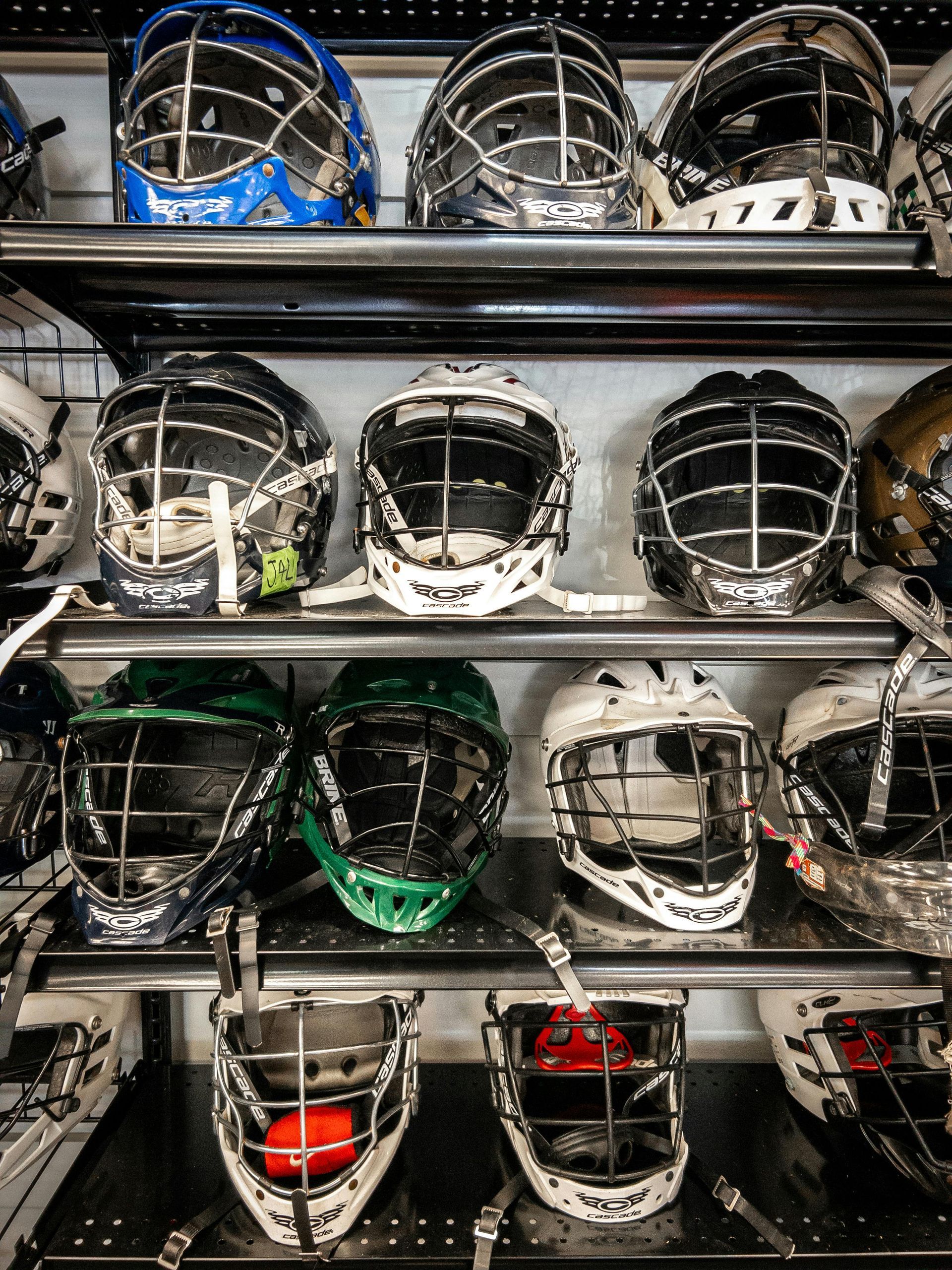 A shelf filled with a variety of lacrosse helmets.