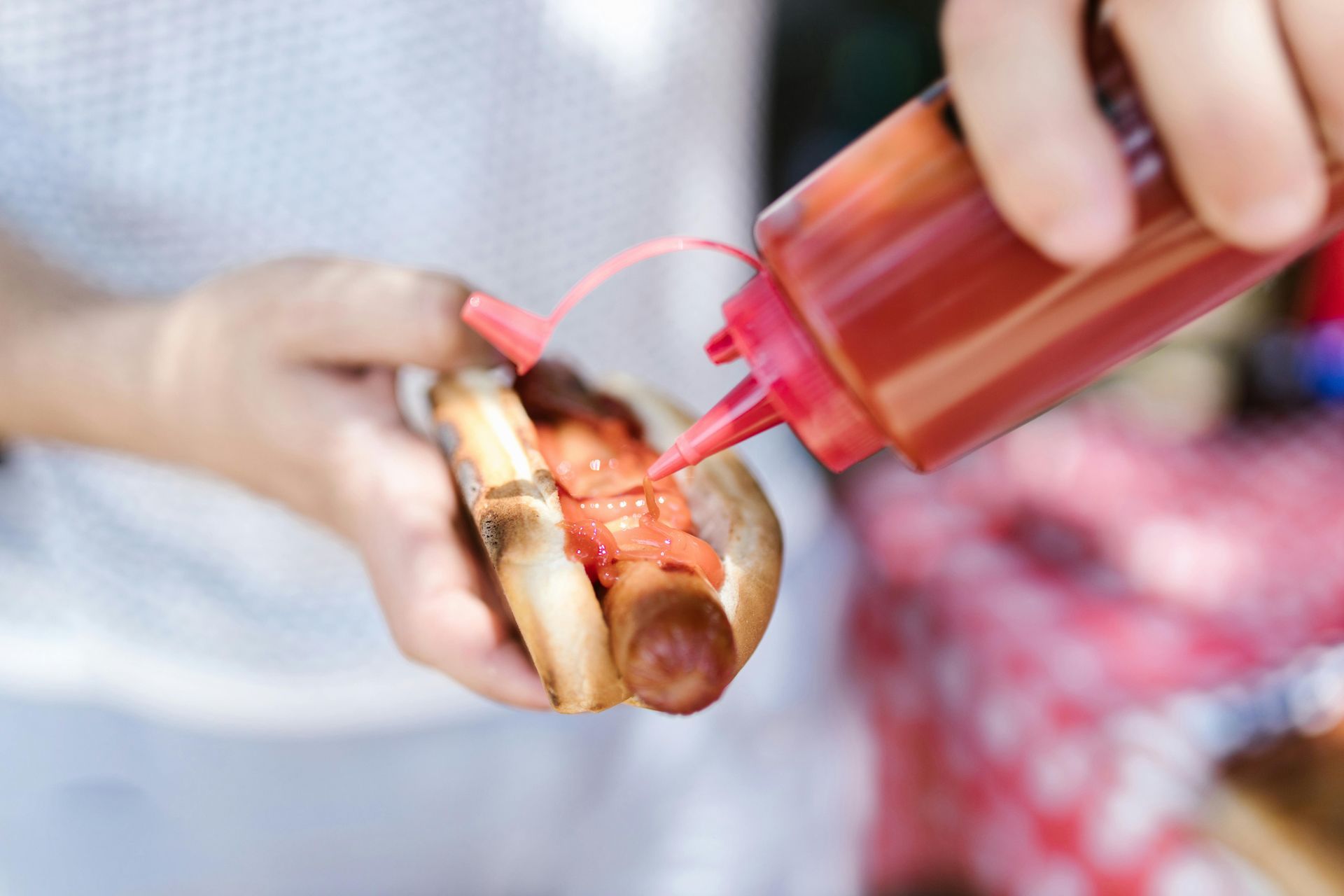 A person is pouring ketchup on a hot dog