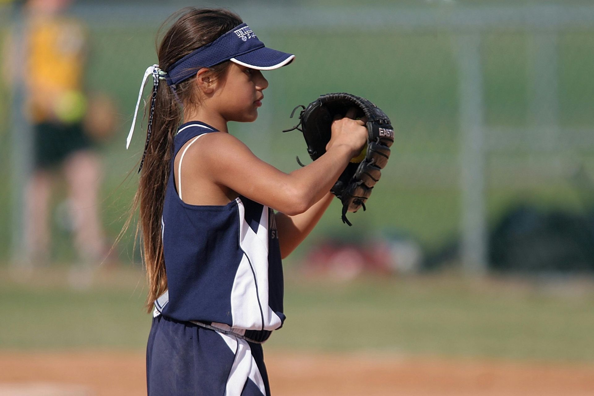 A young girl is holding a baseball glove on a field.