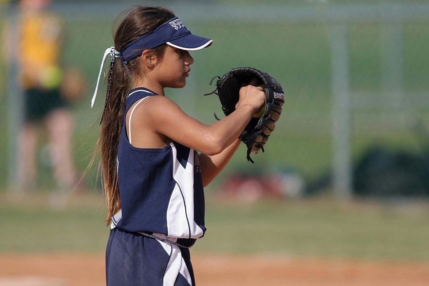 A young girl is holding a baseball glove on a field.