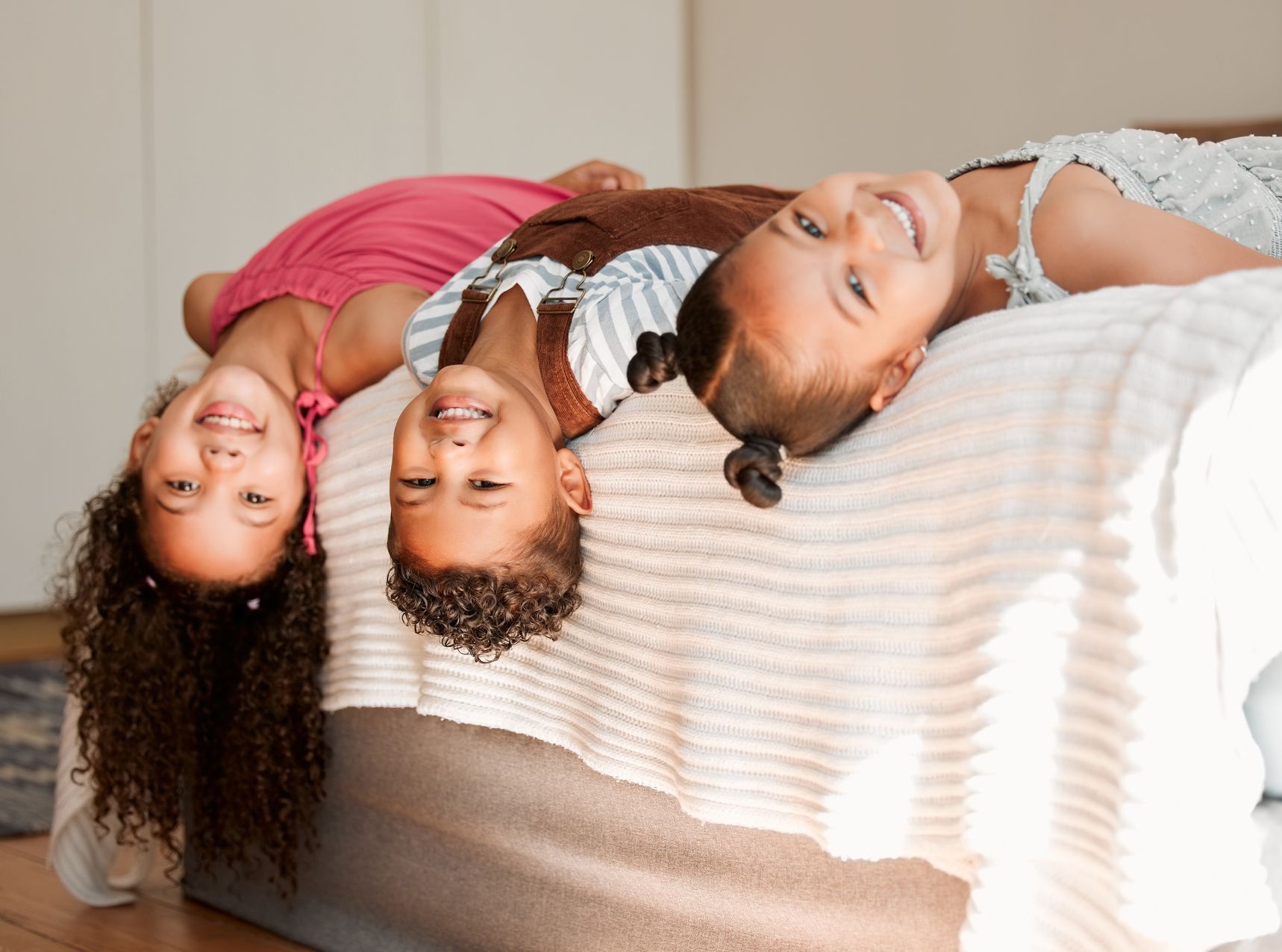 Three young girls are laying upside down on a bed.