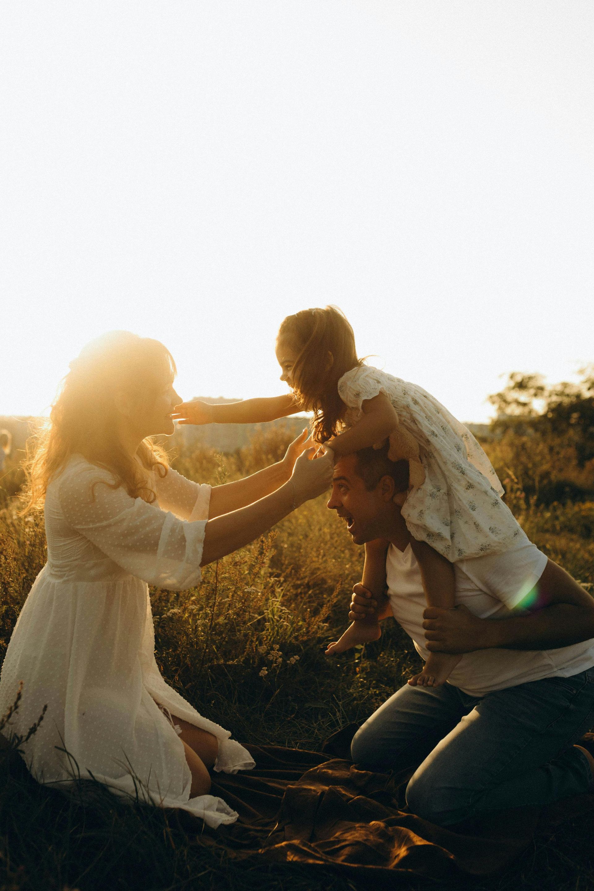 Three people in a sunlit field, laughing and playing together at sunset.