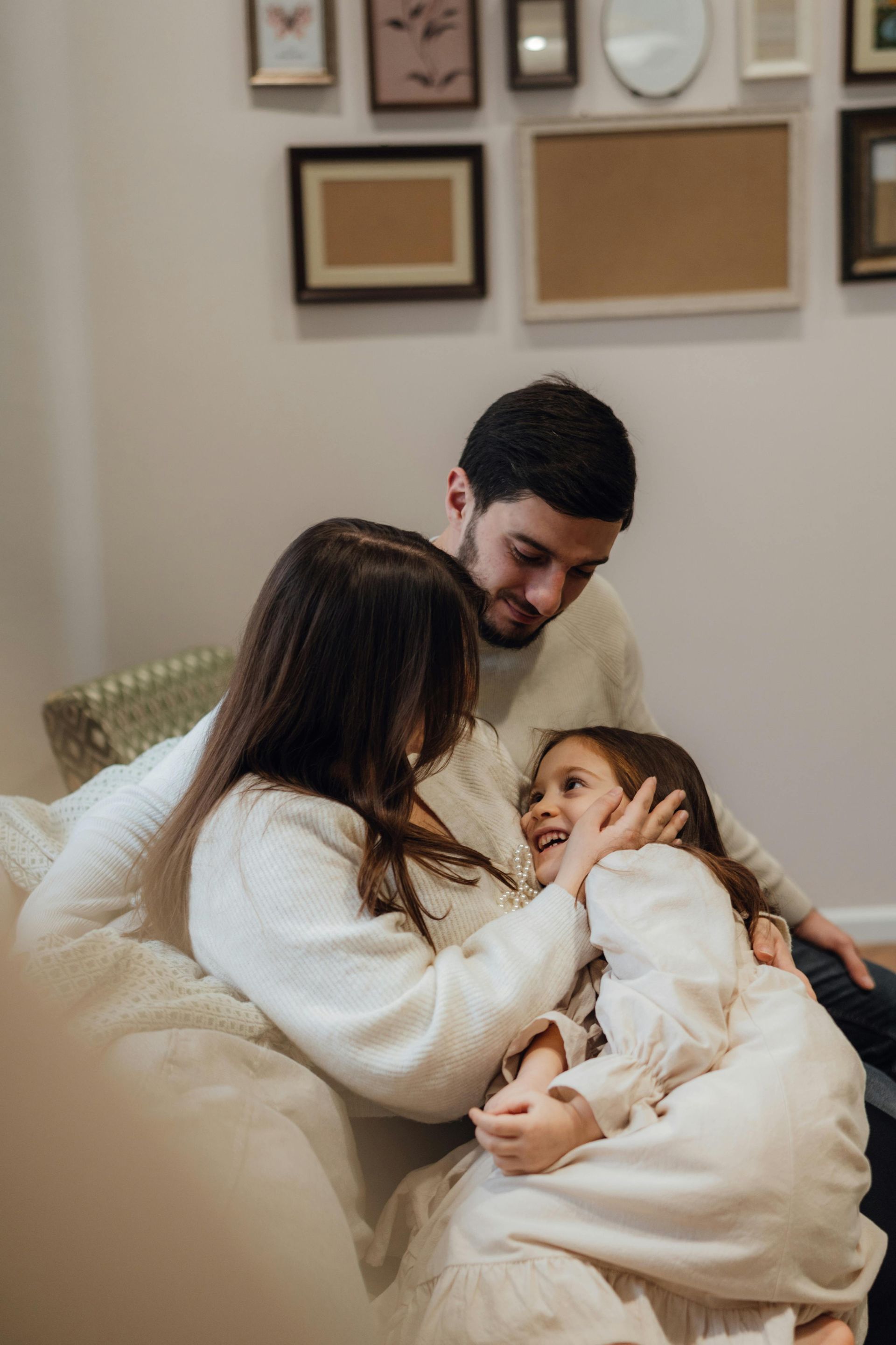 Family sitting on a couch, smiling and cuddling with a baby in a cozy living room.